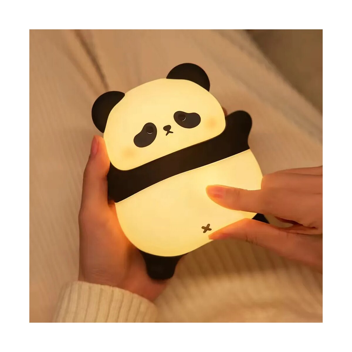 Ein panda-förmiges Nachtlicht, leuchtend, gehalten von Händen. Der Panda hat schwarz-weißes Fell.