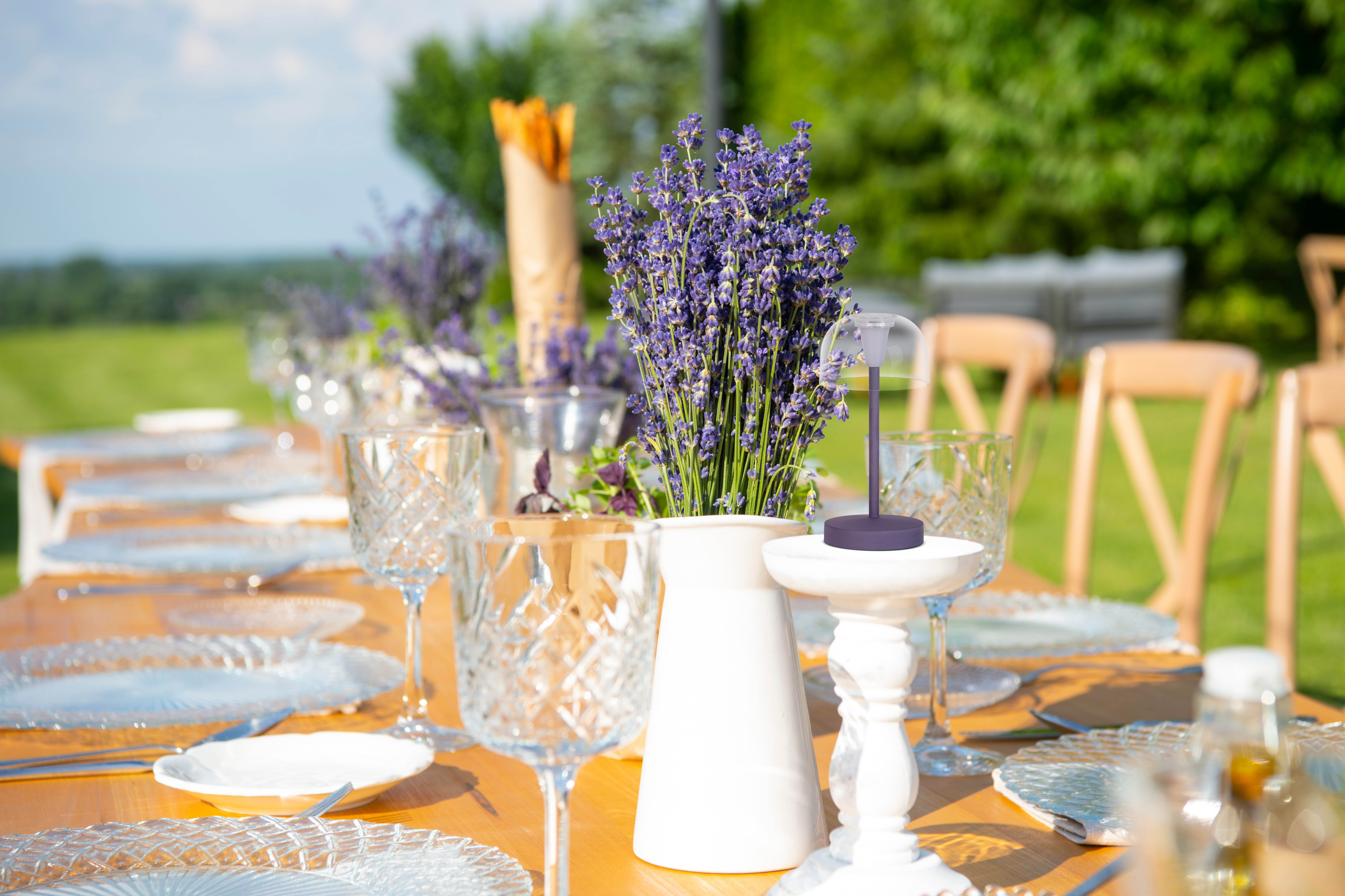 Gedeckter Tisch im Freien mit Lavendelstrauß, Gläsern und Tellern.