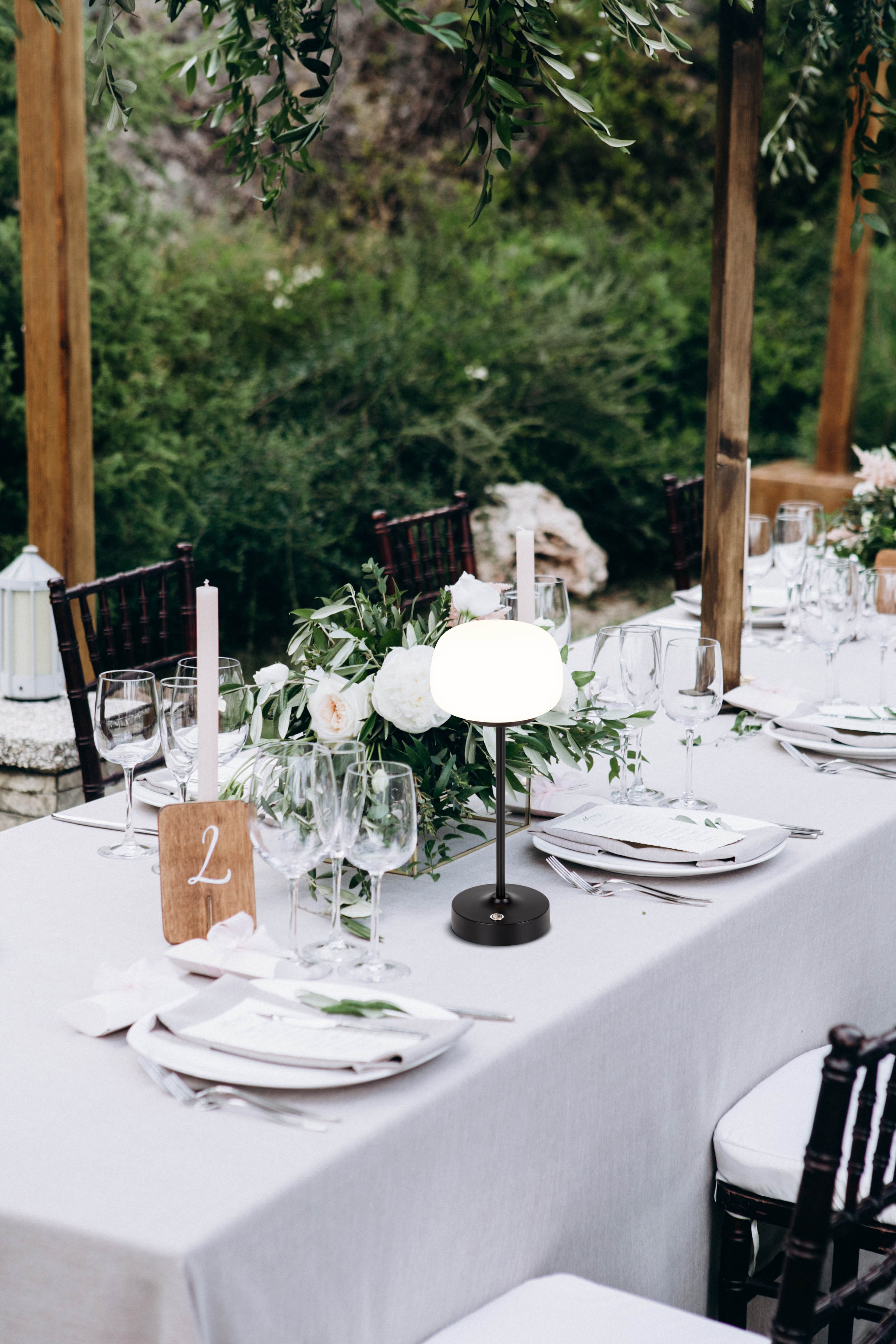 Ein Tisch für eine Outdoor-Veranstaltung. Der Tisch hat eine weiße Tischdecke und ist mit Blumen und Kerzen dekoriert.