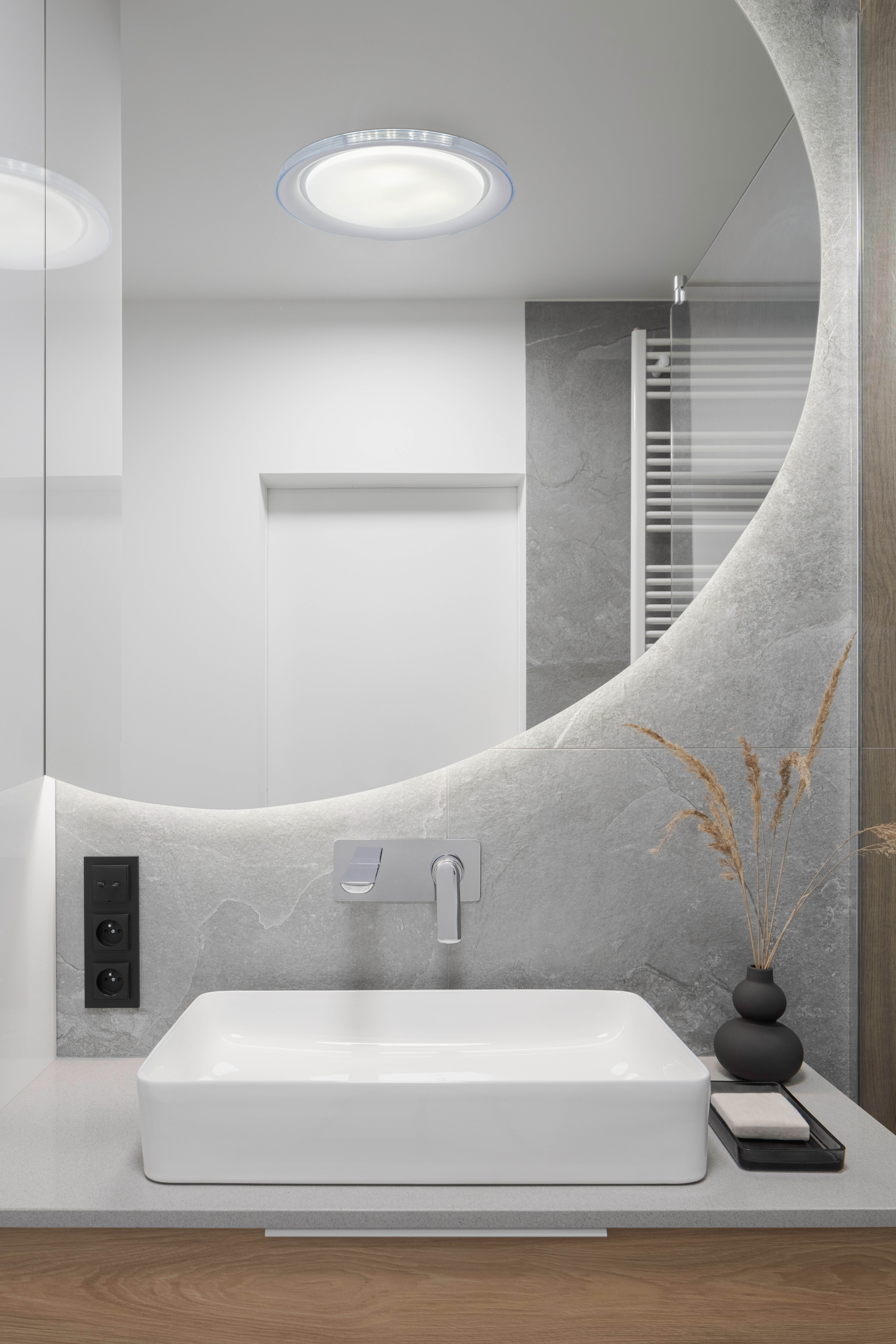 Badezimmer mit großem Spiegel über einem weißen Waschbecken und einer kleinen schwarzen Steckdose.