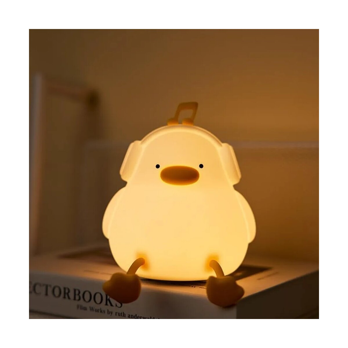 Eine gelbe Entenlampe sitzt auf einem Buch und wirft einen warmen Schein in einen dunklen Raum.