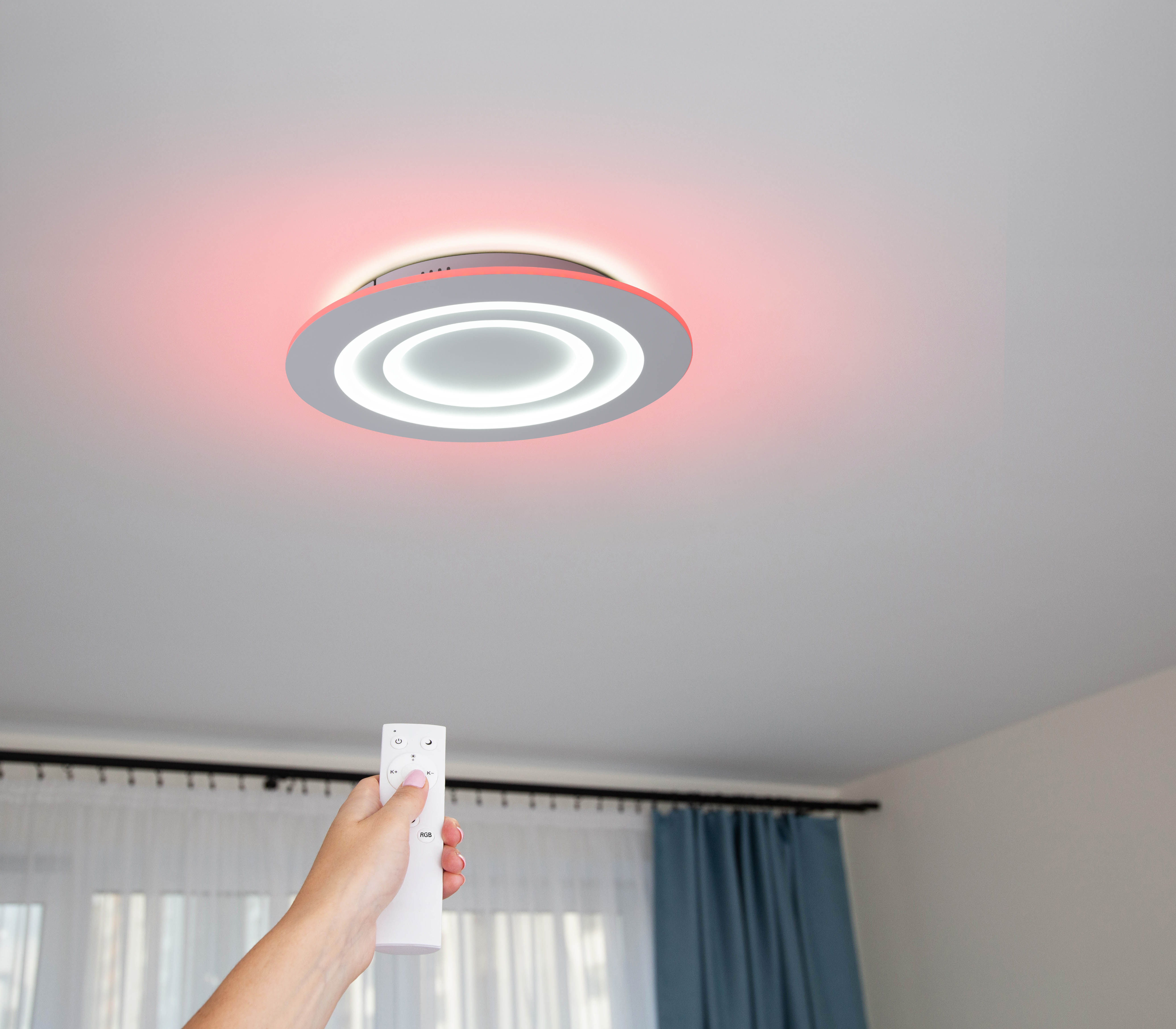 Eine Person hält eine Fernbedienung, mit einer Deckenleuchte mit rotem Ring.