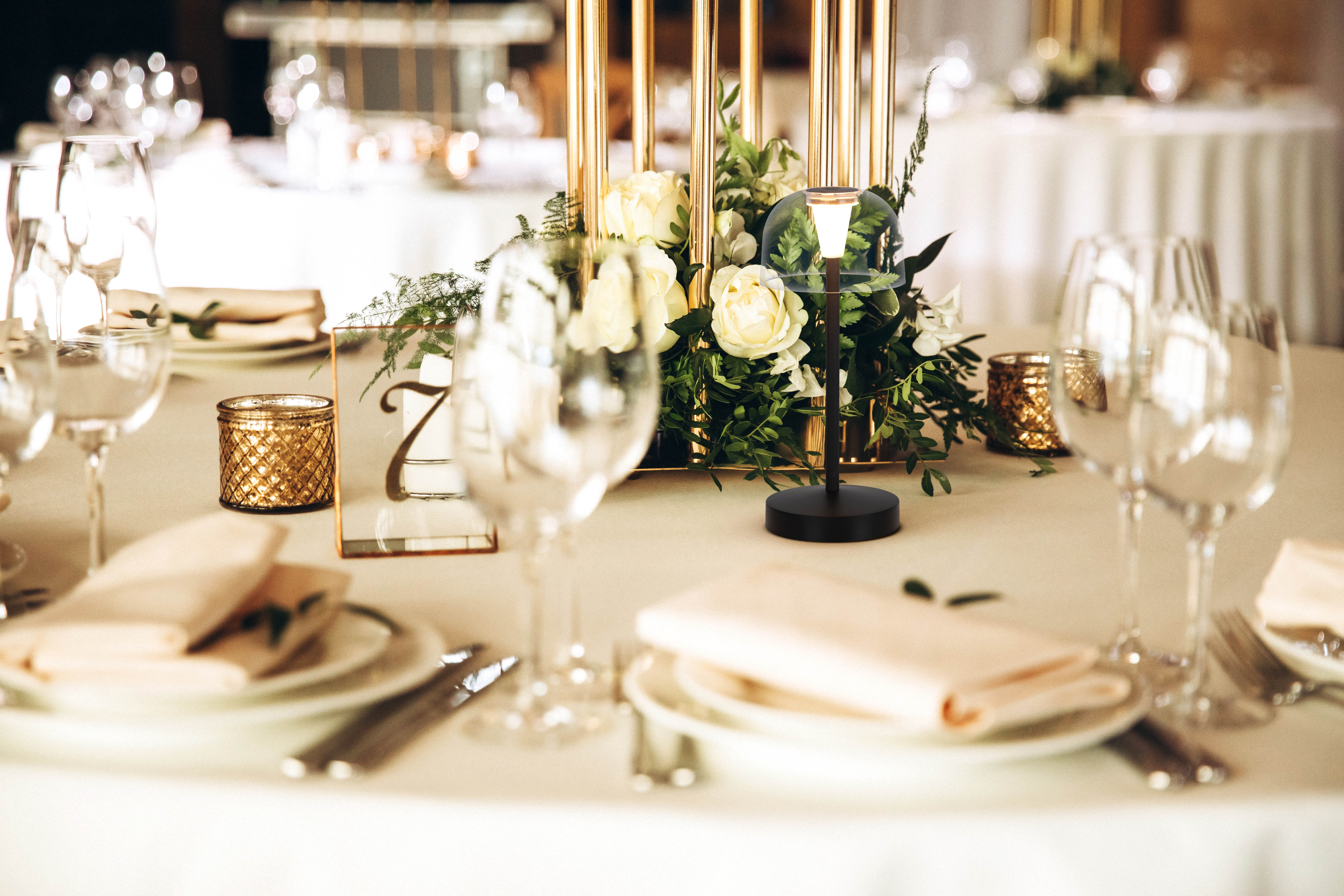 Elegante Tischdekoration mit Blumen, Gläsern und einer brennenden Kerze.