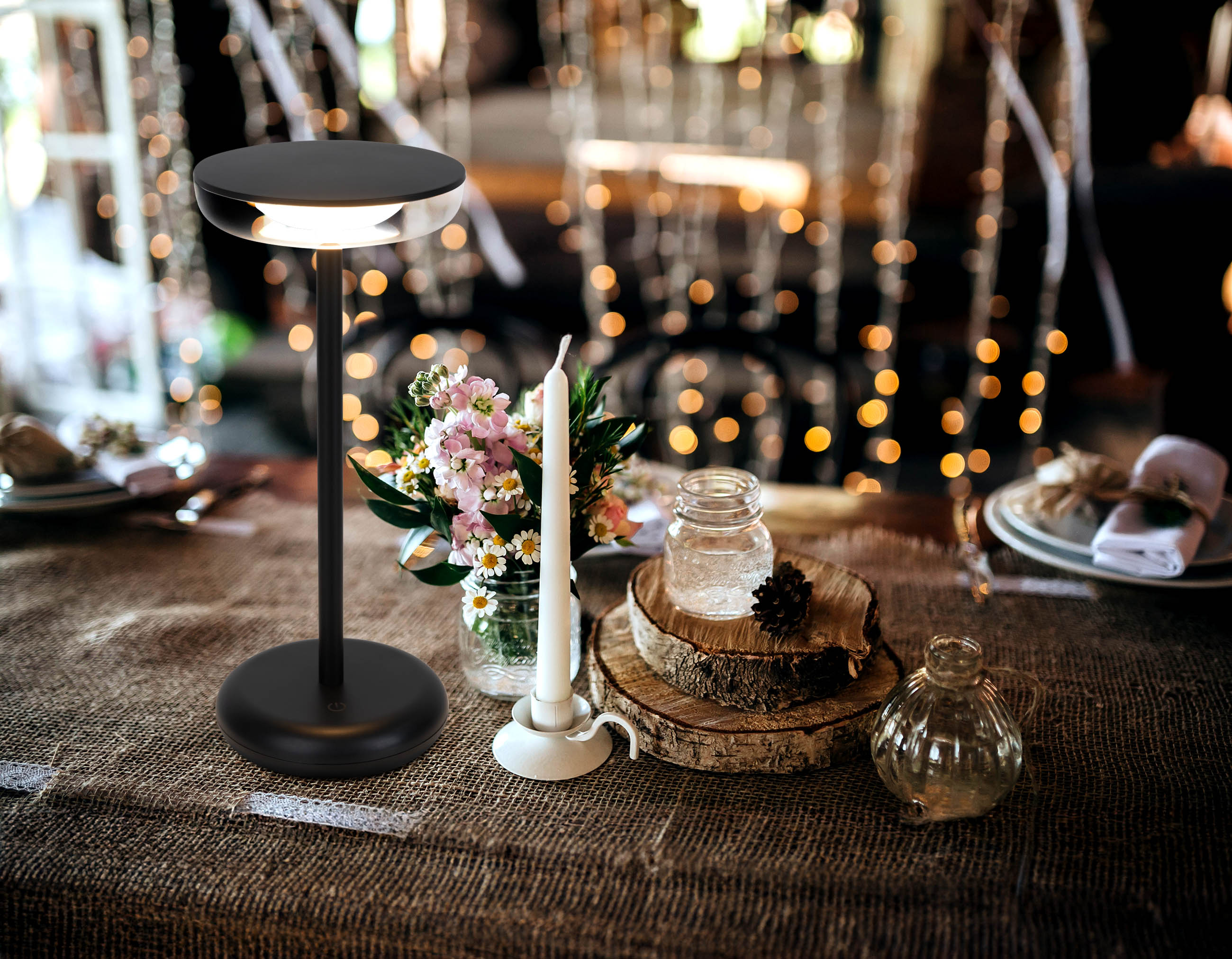 Schwarze Tischlampe mit Kerze, Blumen und Dekorationen auf einem Tisch.