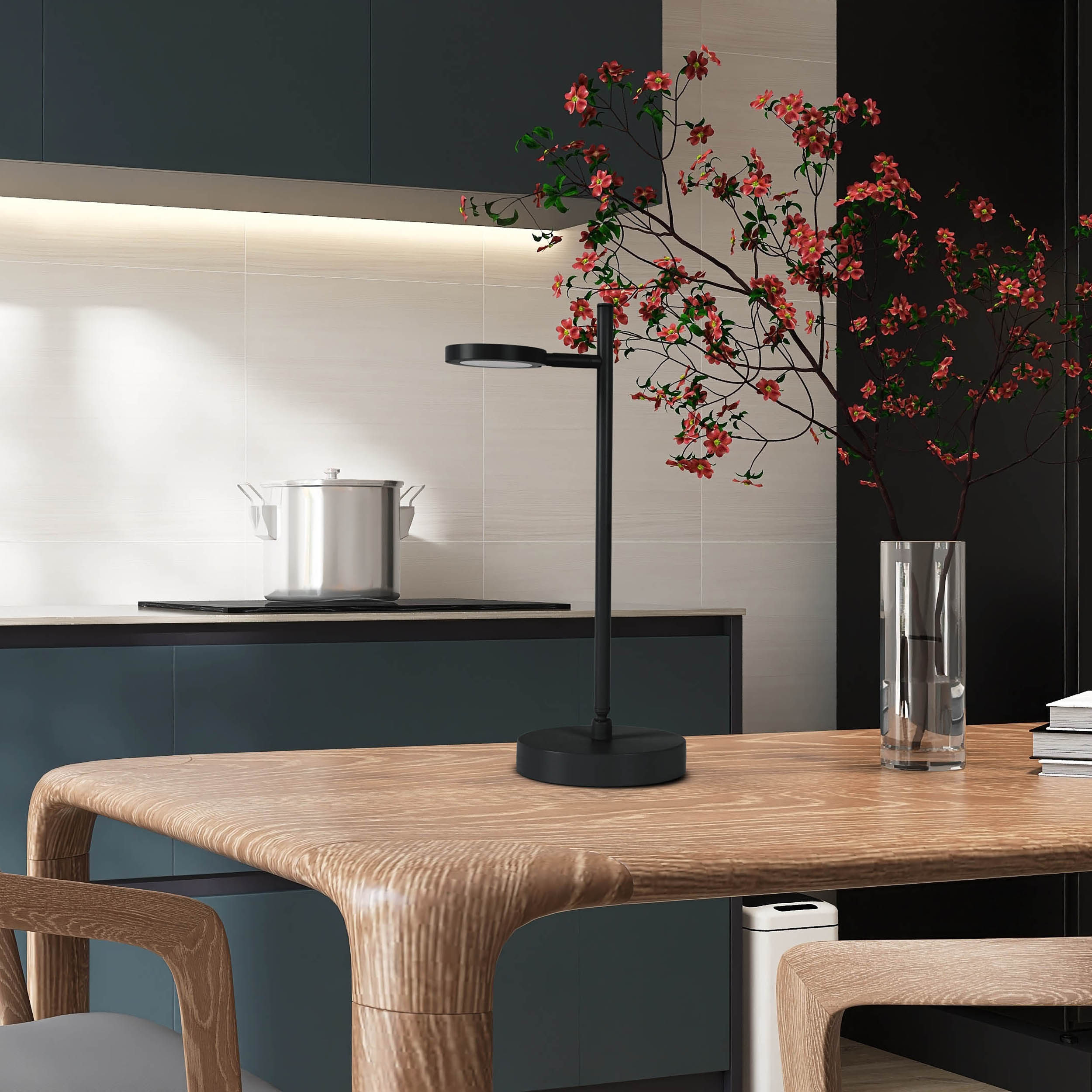 Eine schwarze Schreibtischlampe mit schwarzem Sockel. Eine Vase mit roten Blumen. Ein Holztisch.