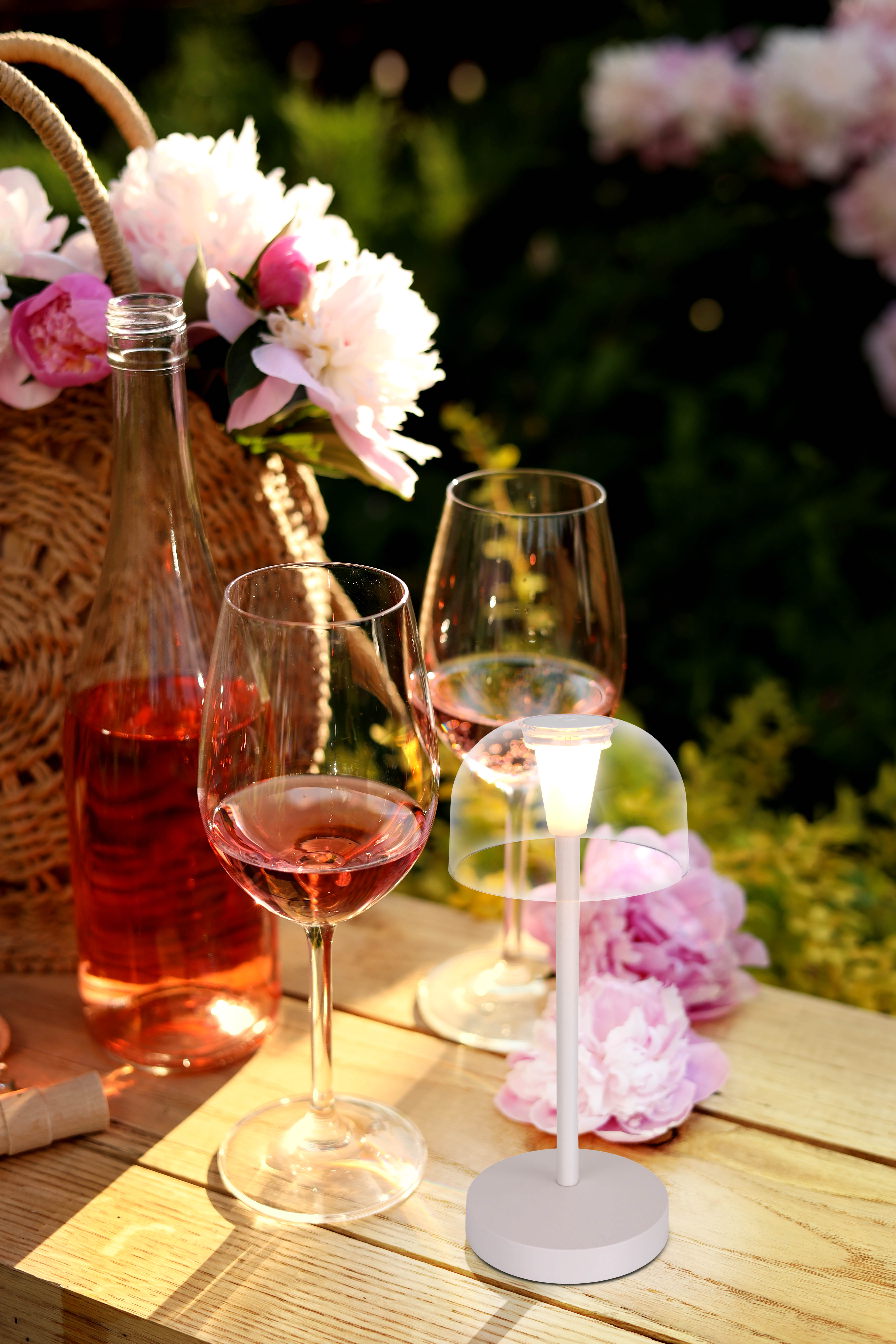 Eine Picknick-Szene mit Weingläsern, einer Tischlampe, Blumen und einem Korb.