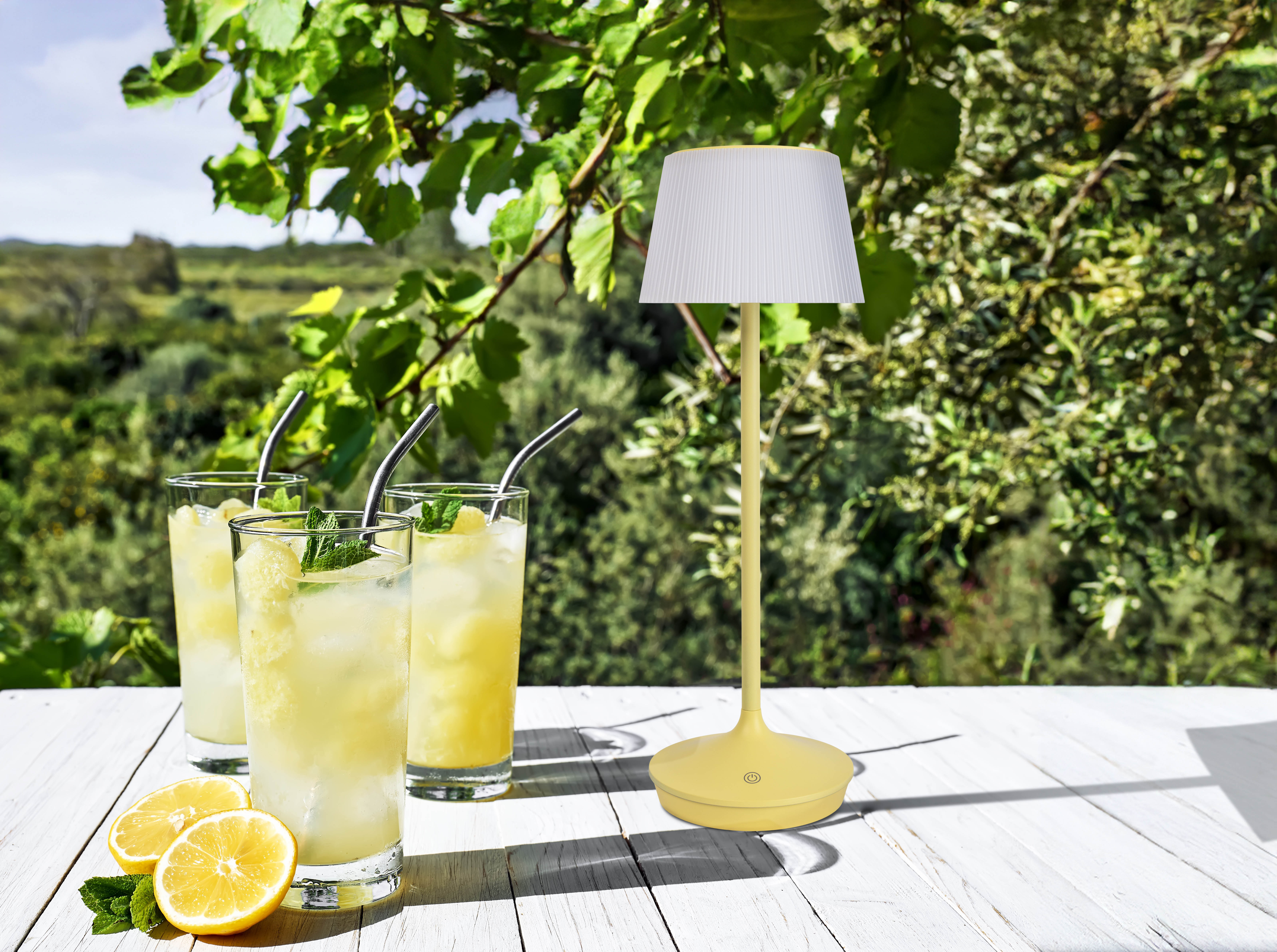 Gelbe Lampe auf einem weißen Tisch mit Getränken und Zitronen. Grüner Hintergrund.