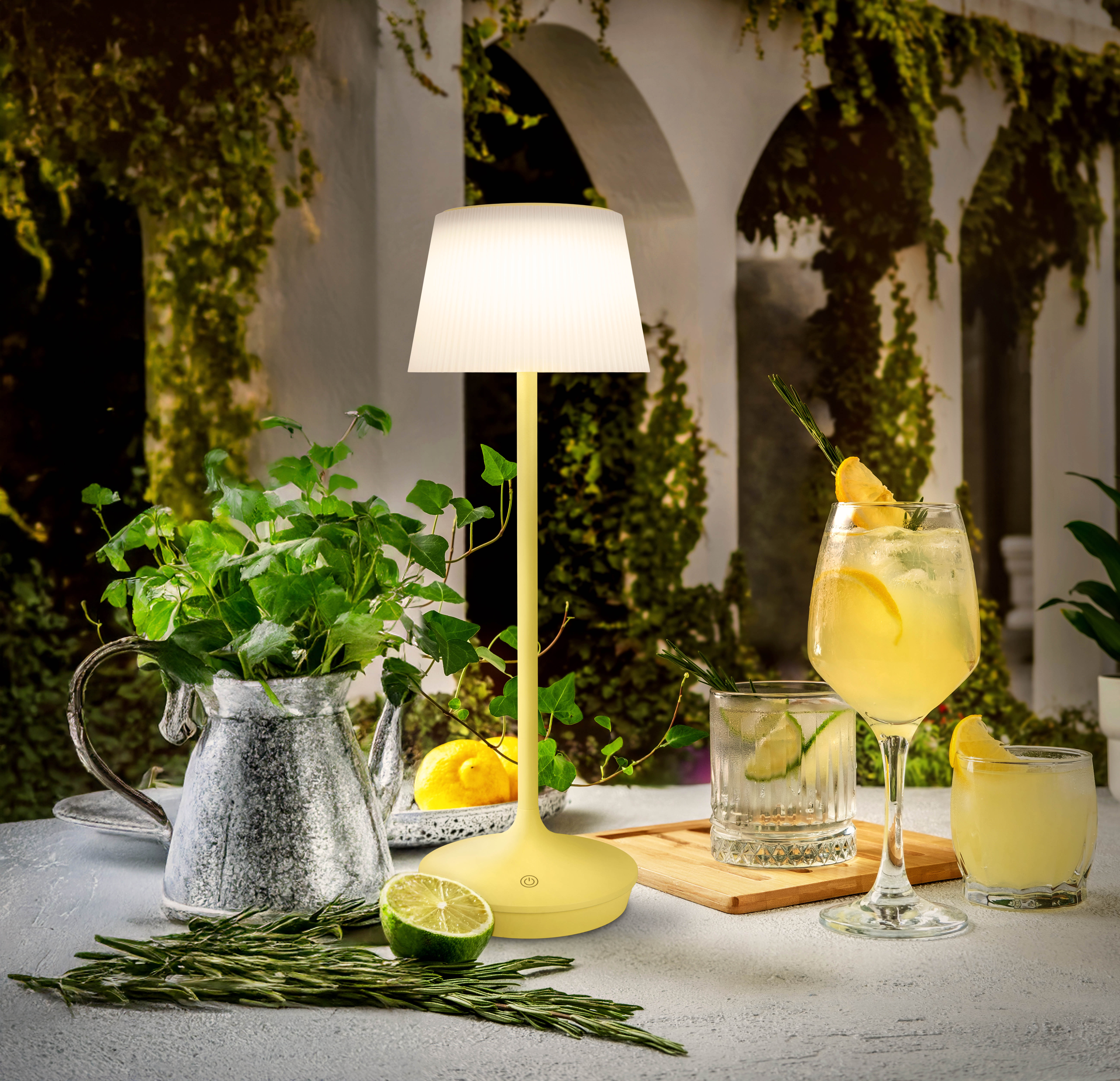Tischlampe mit gelbem Fuß und Schirm, mit Getränken und Pflanzen auf dem Tisch.