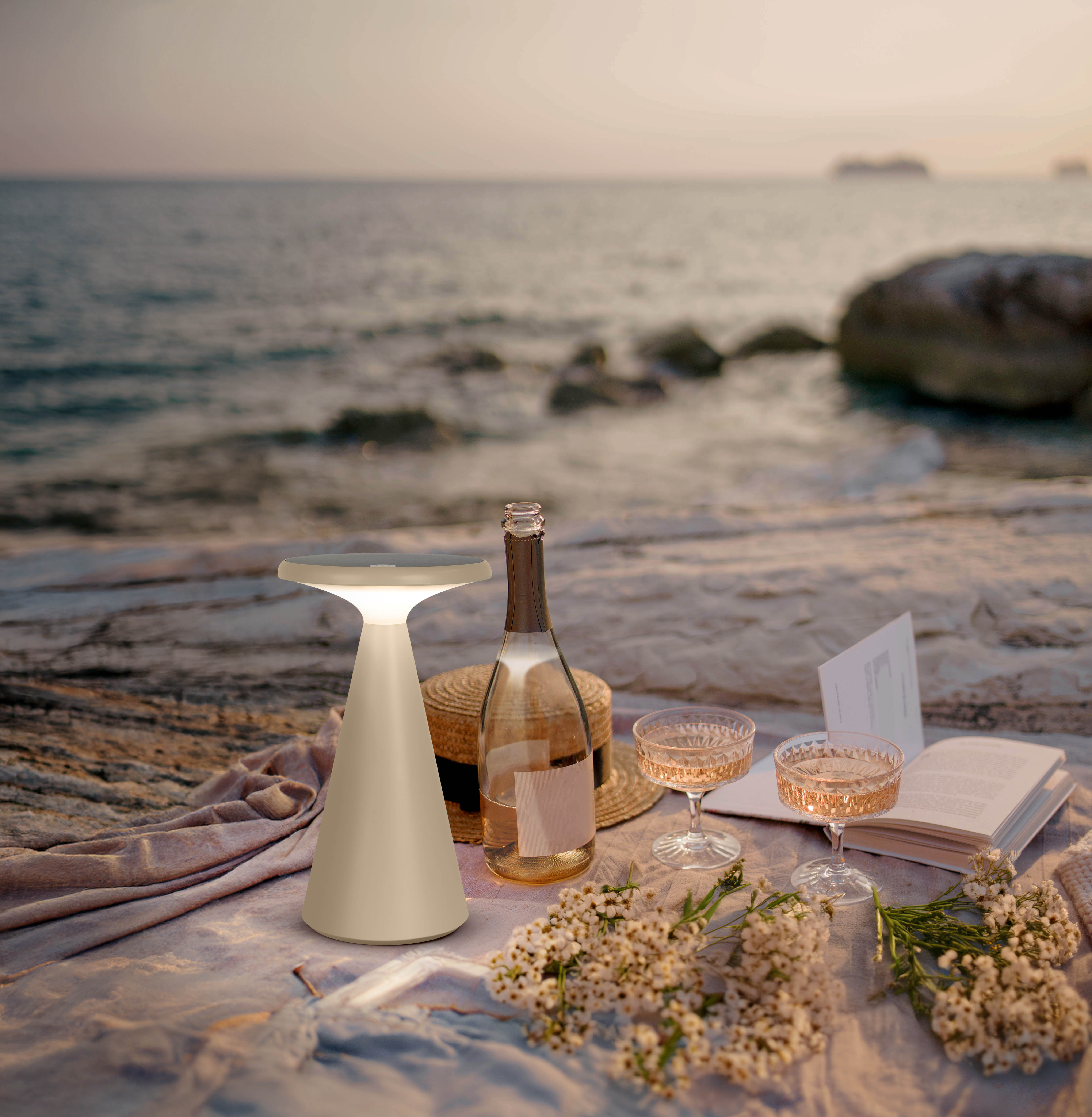 Strandpicknick mit Lampe, Flasche, Gläsern, Hut und Buch am Meer.