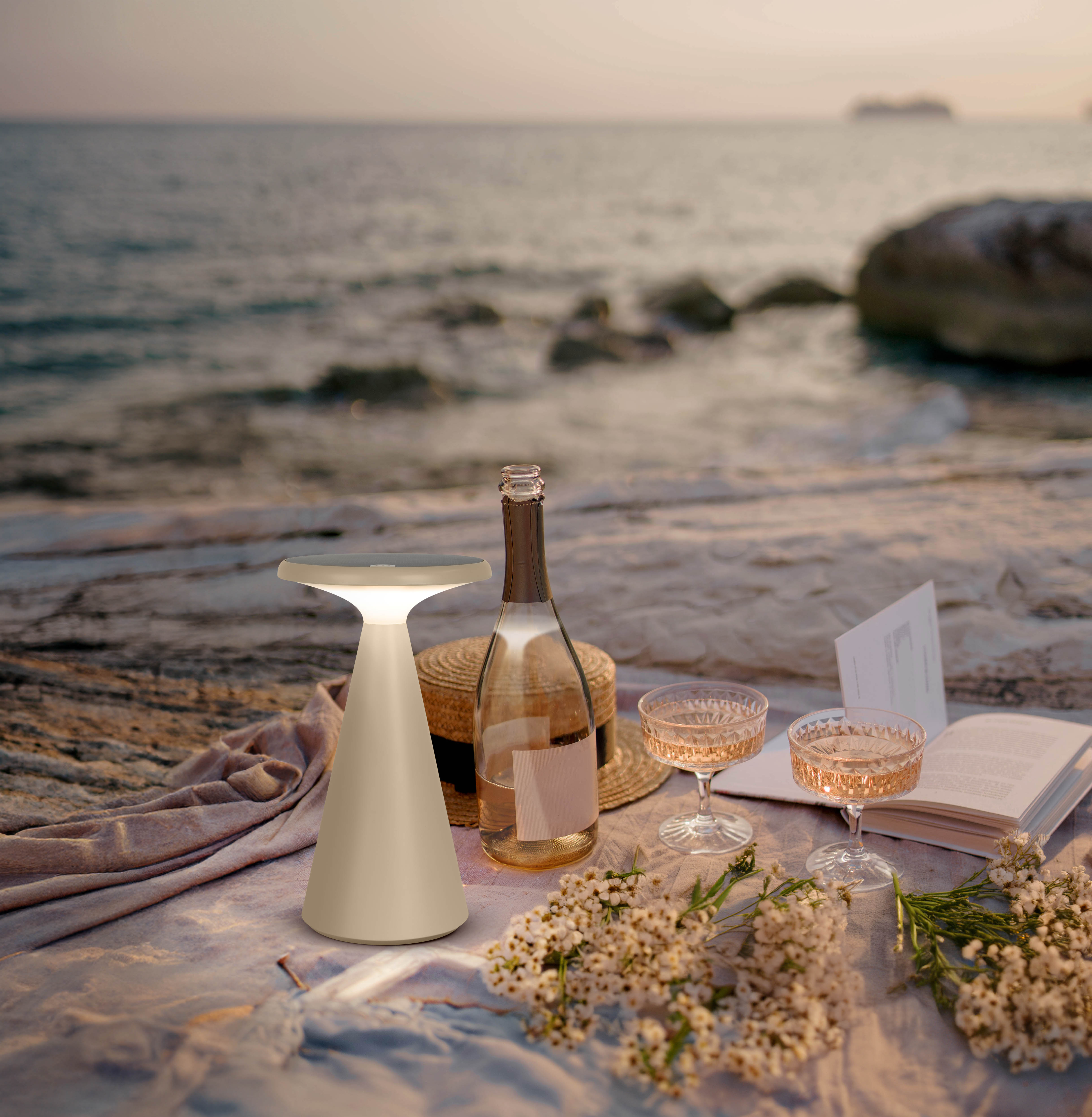 Eine weiße Lampe auf einem Tisch, Strand im Hintergrund, mit Getränken und Blumen.