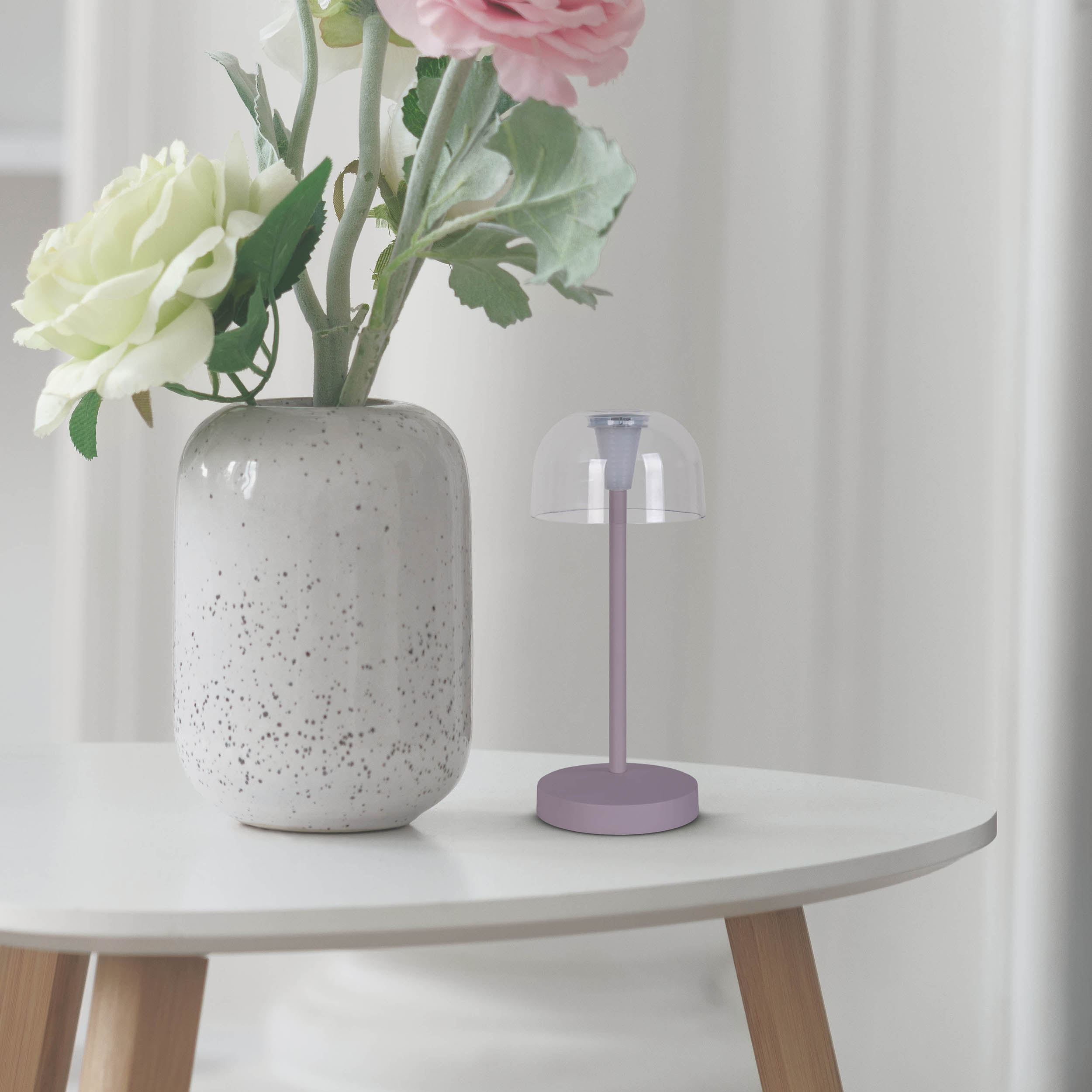 Una piccola lampada viola e un vaso con fiori su un tavolo rotondo bianco.