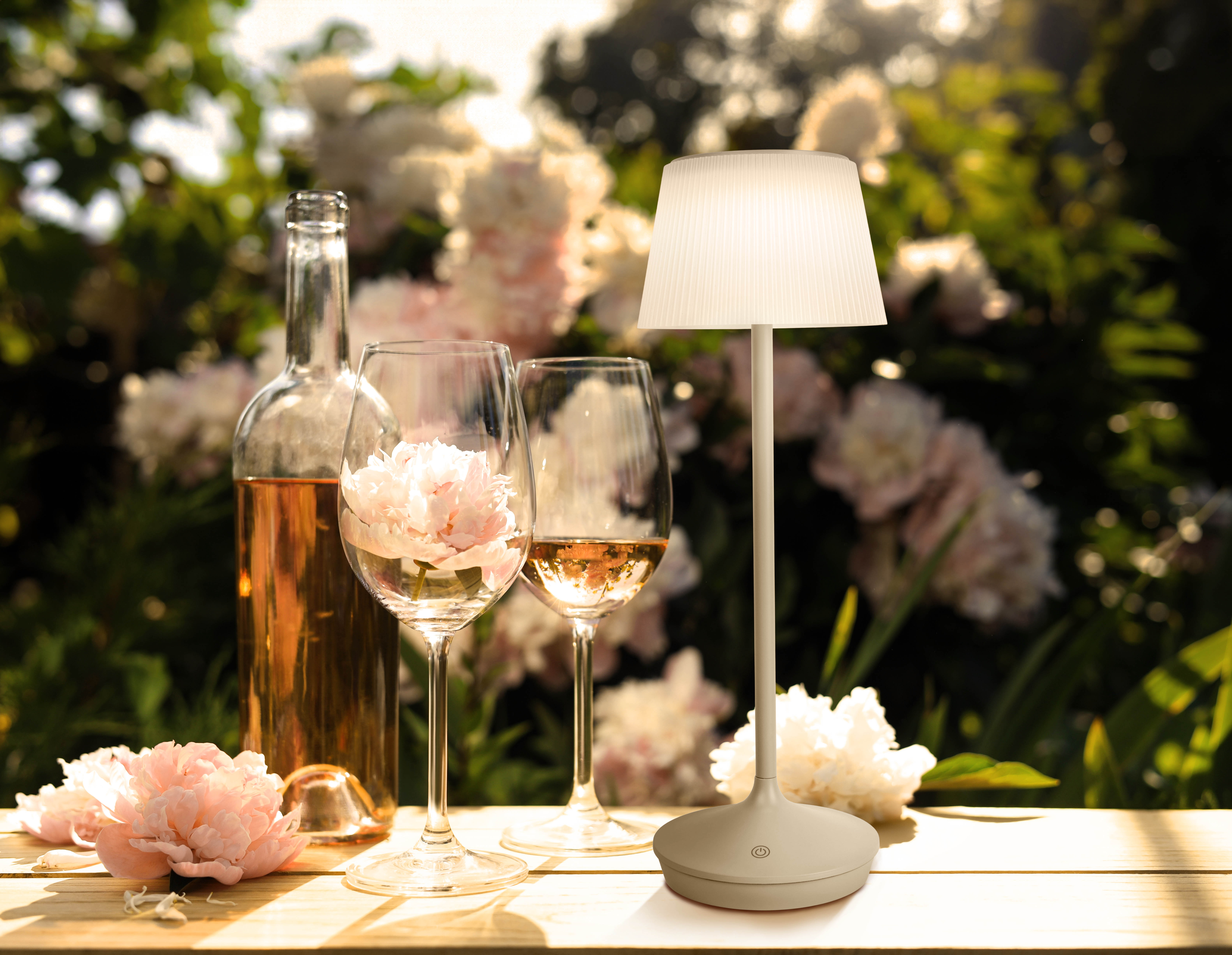 Eine Lampe mit Weingläsern und Flasche in einem Garten mit Blumen und Grün.
