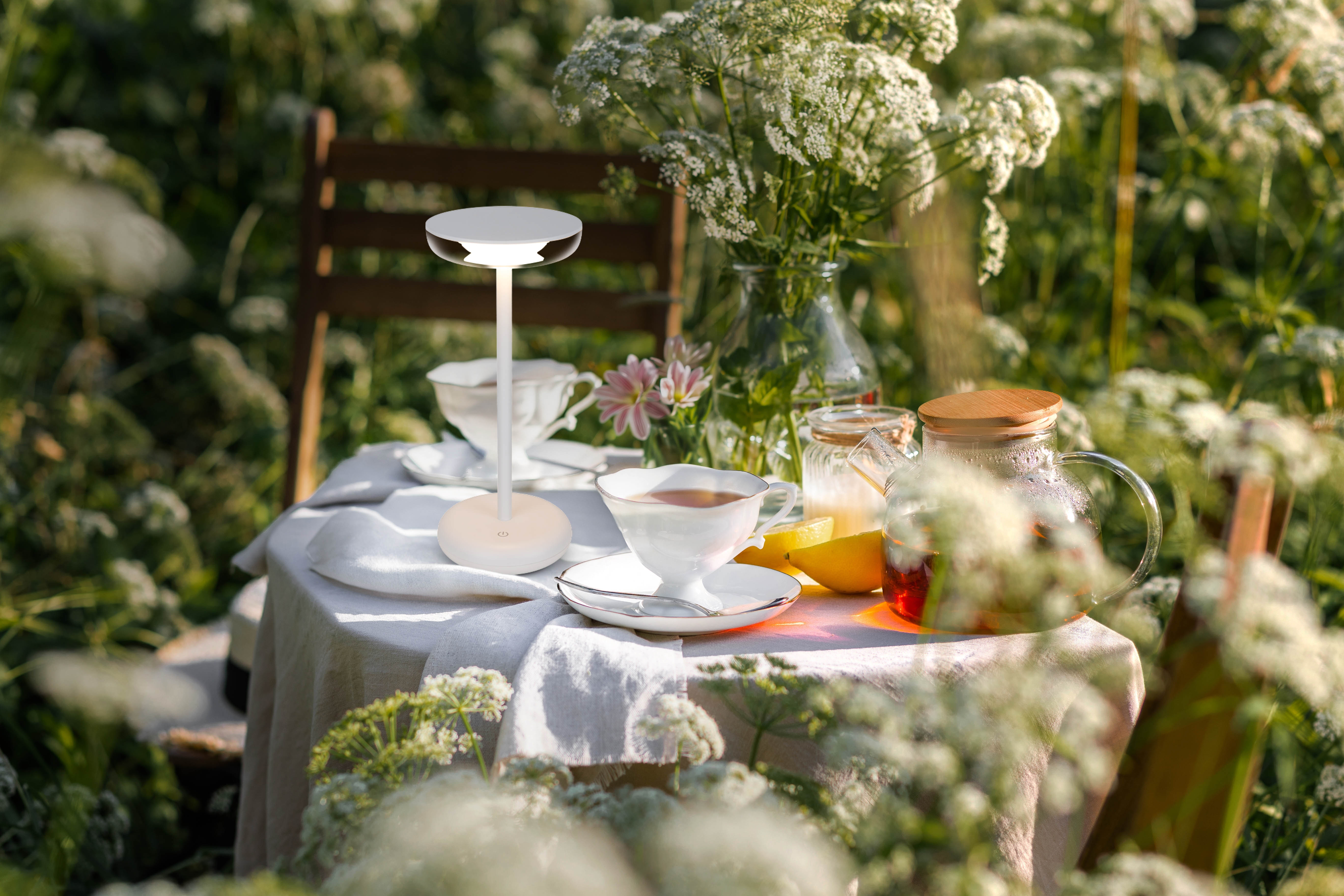 Eine Tischdekoration in einem Garten mit Tee, Blumen und einer modernen Lampe.