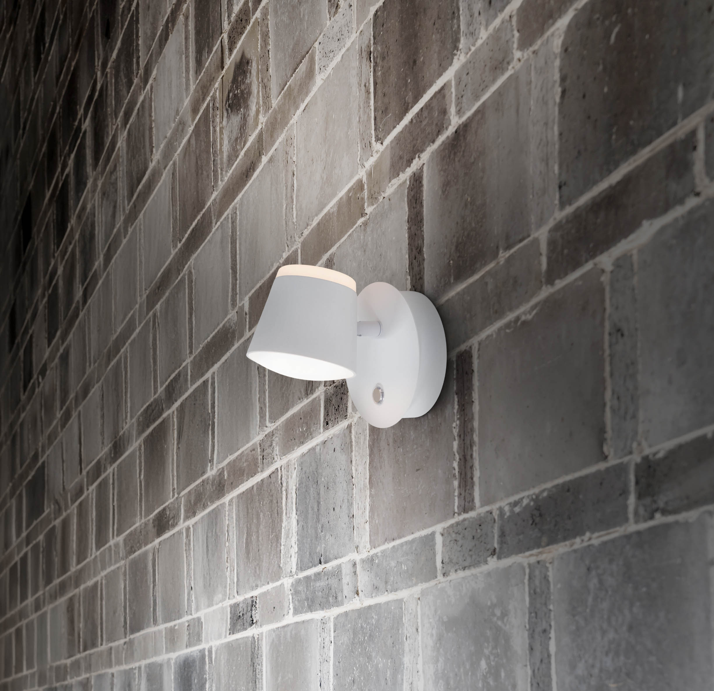 Eine weiße Außenlampe an einer Ziegelmauer. Das Licht scheint nach unten. Die Lampe ist an der Wand montiert.