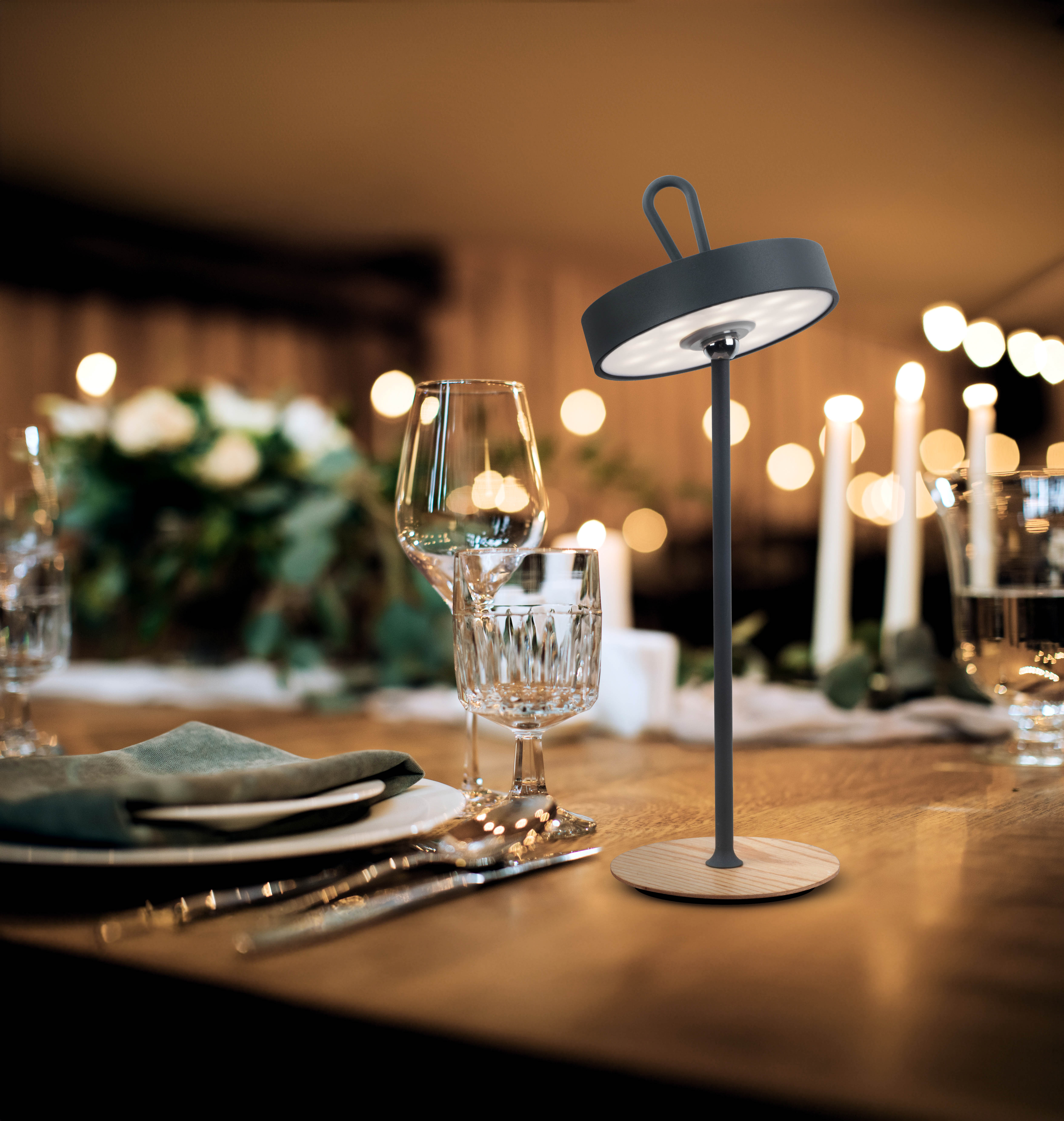 Eine moderne Lampe mit dunkelgrauem Schirm und Holzfuß, auf einem Tisch mit anderen Gegenständen.