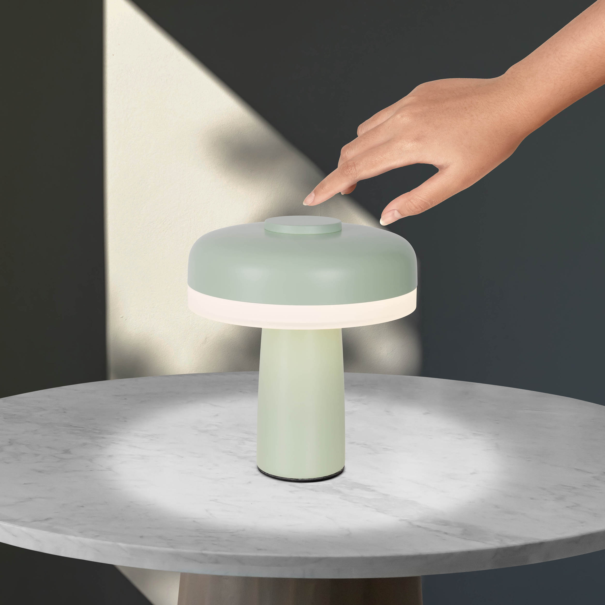 Eine mintgrüne Lampe mit weißem Licht und rundem Aufsatz. Eine Hand berührt die Oberseite.