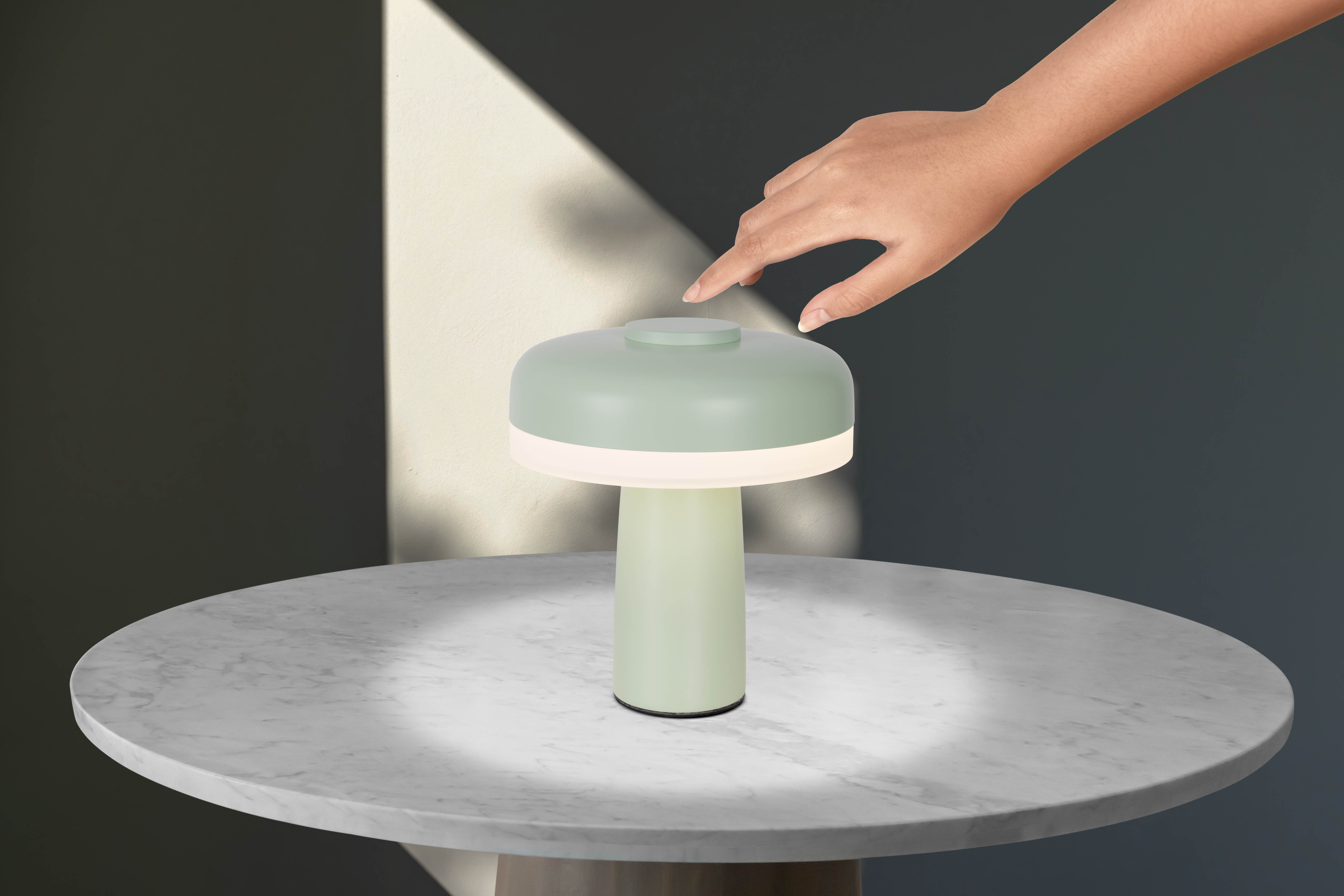 Eine grün-weiße pilzförmige Lampe, mit einer Hand, die die Oberseite berührt.