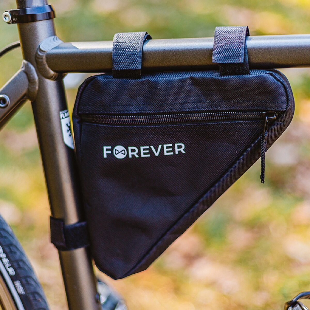 Eine schwarze, dreieckige Tasche, die an einem Fahrradrahmen befestigt ist, mit der Aufschrift 'FOREVER'. Sie befindet sich an einem Fahrrad.