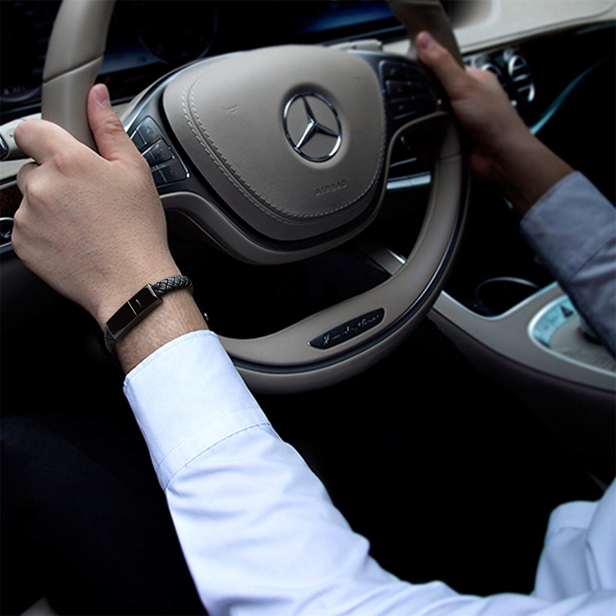 Männerhände an einem Lenkrad mit einem Armband. Das Armband ist schwarz und silber.