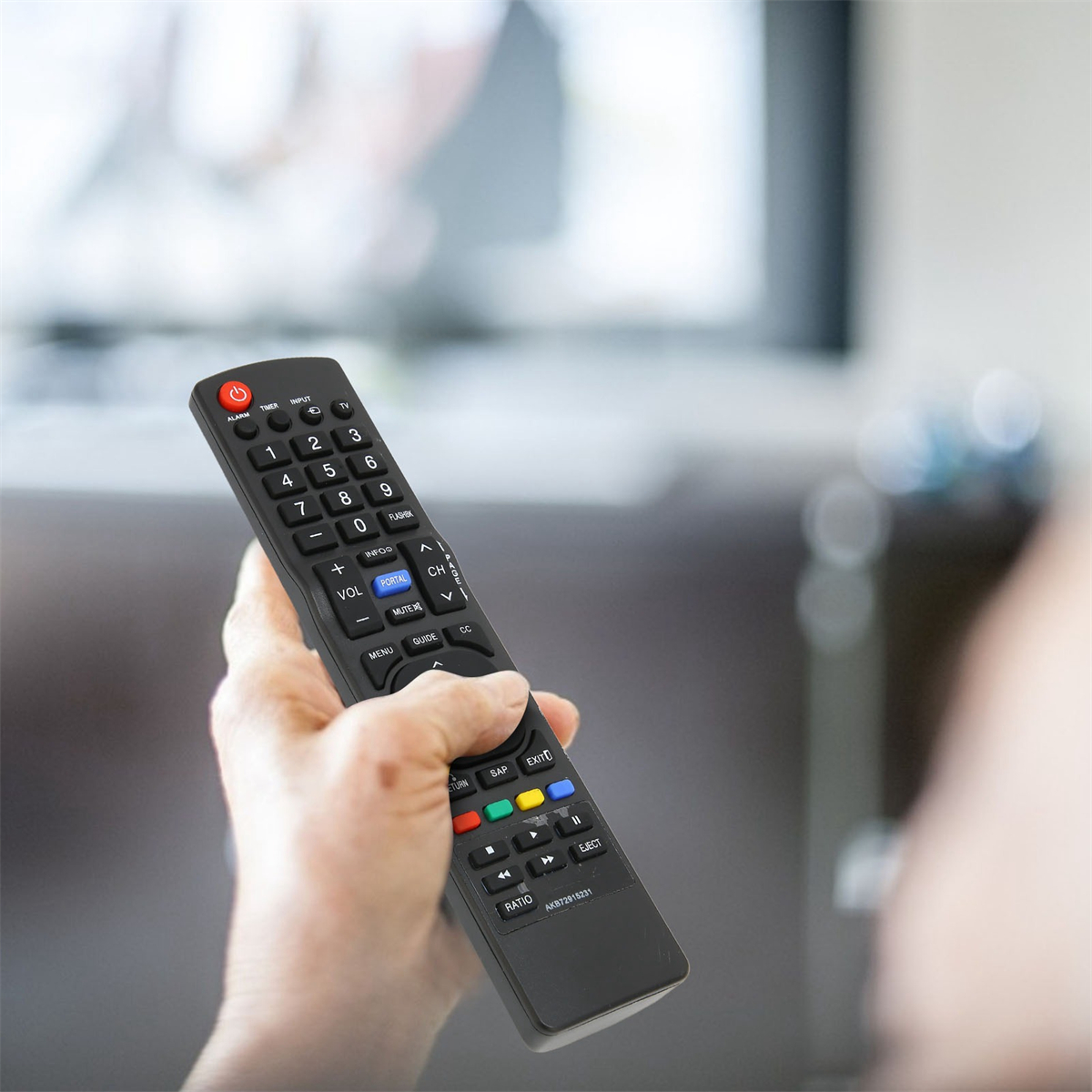 Eine Hand hält eine schwarze TV-Fernbedienung. Im Hintergrund ist eine Person mit einem unscharfen Fernsehbildschirm.