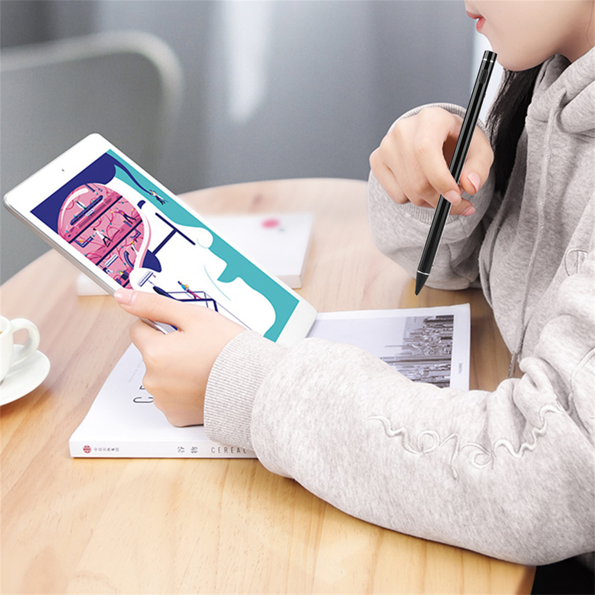 Eine Person, die einen Stift auf einem Tablet zum Zeichnen verwendet, mit einem Buch und Kaffee im Blick.