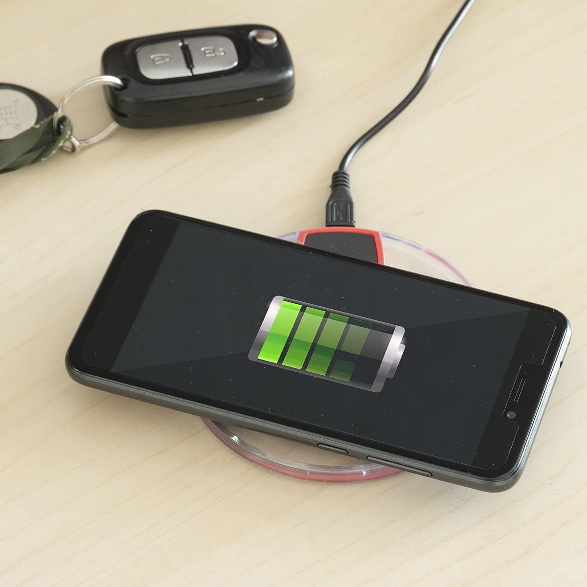 Schwarzes Telefon, das drahtlos auf einem Pad, Schlüssel und Autoschlüssel geladen wird.