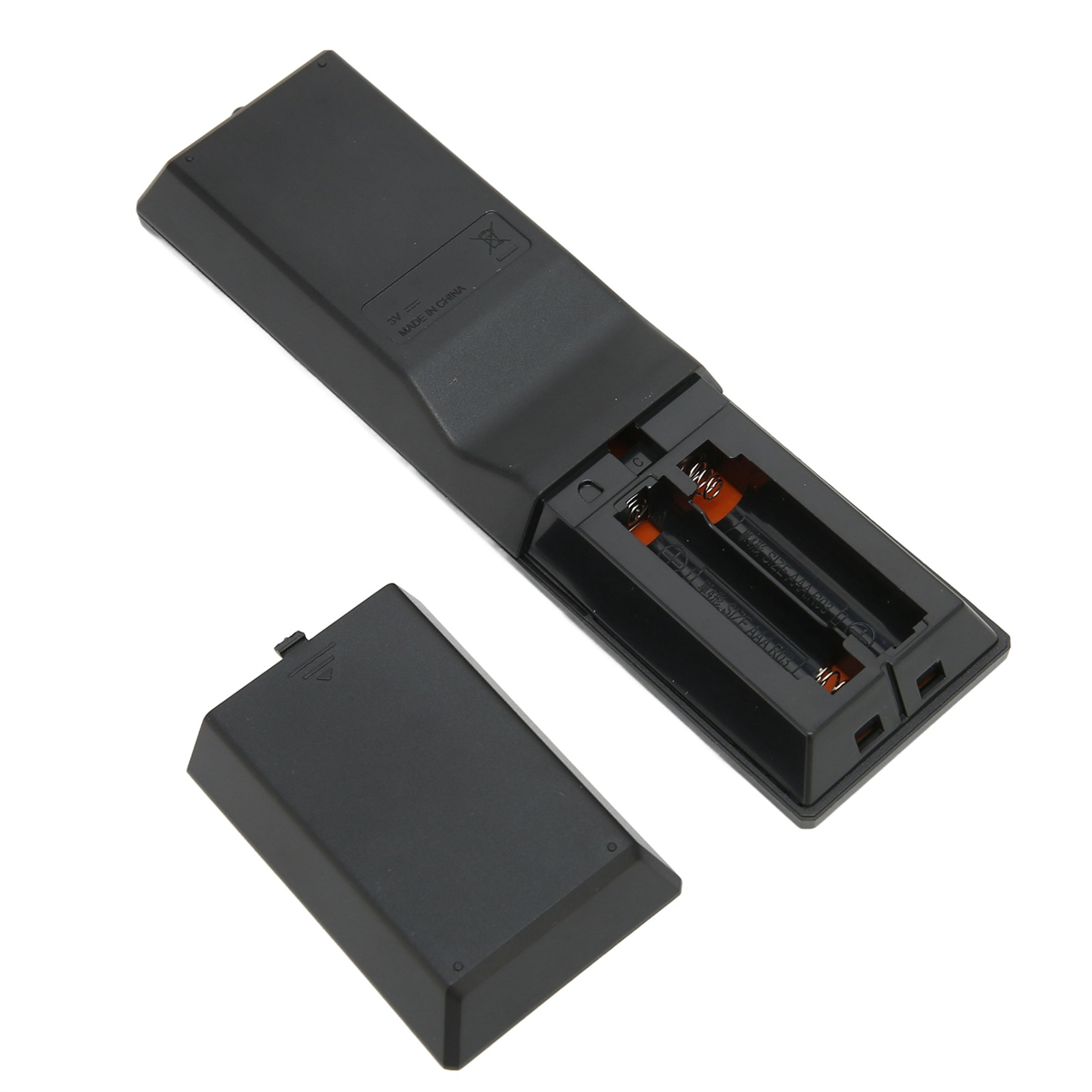 Rückseite einer schwarzen Fernbedienung mit geöffnetem Batteriefach, das Batterien zeigt. Ein abgenommener Batteriedeckel liegt daneben.