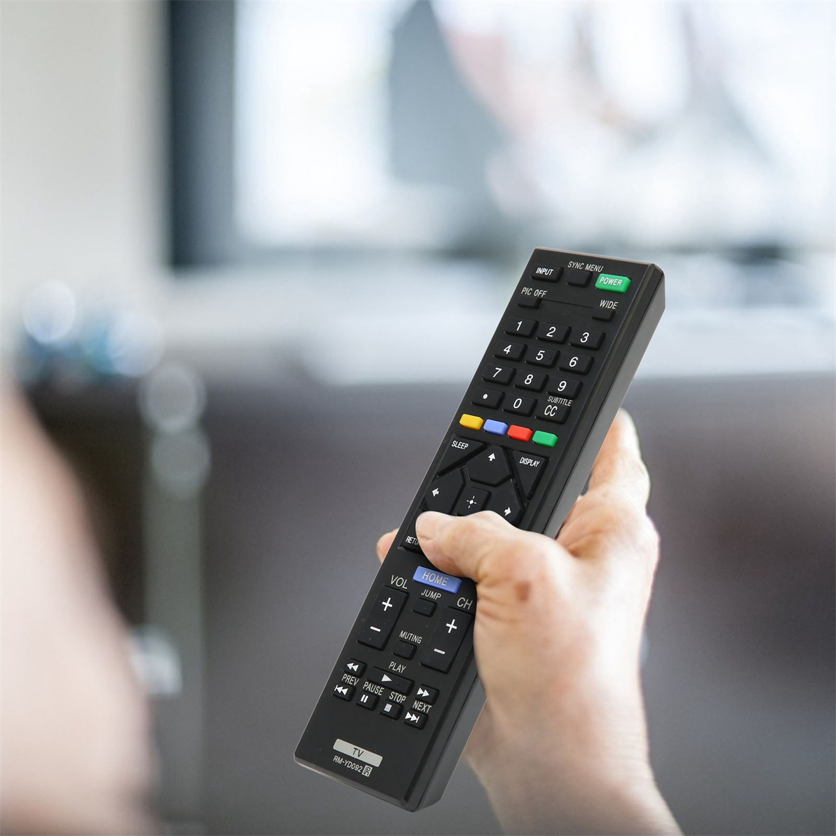 Eine Hand hält eine schwarze Fernbedienung mit verschiedenen Knöpfen, zeigt auf einen TV-Bildschirm.