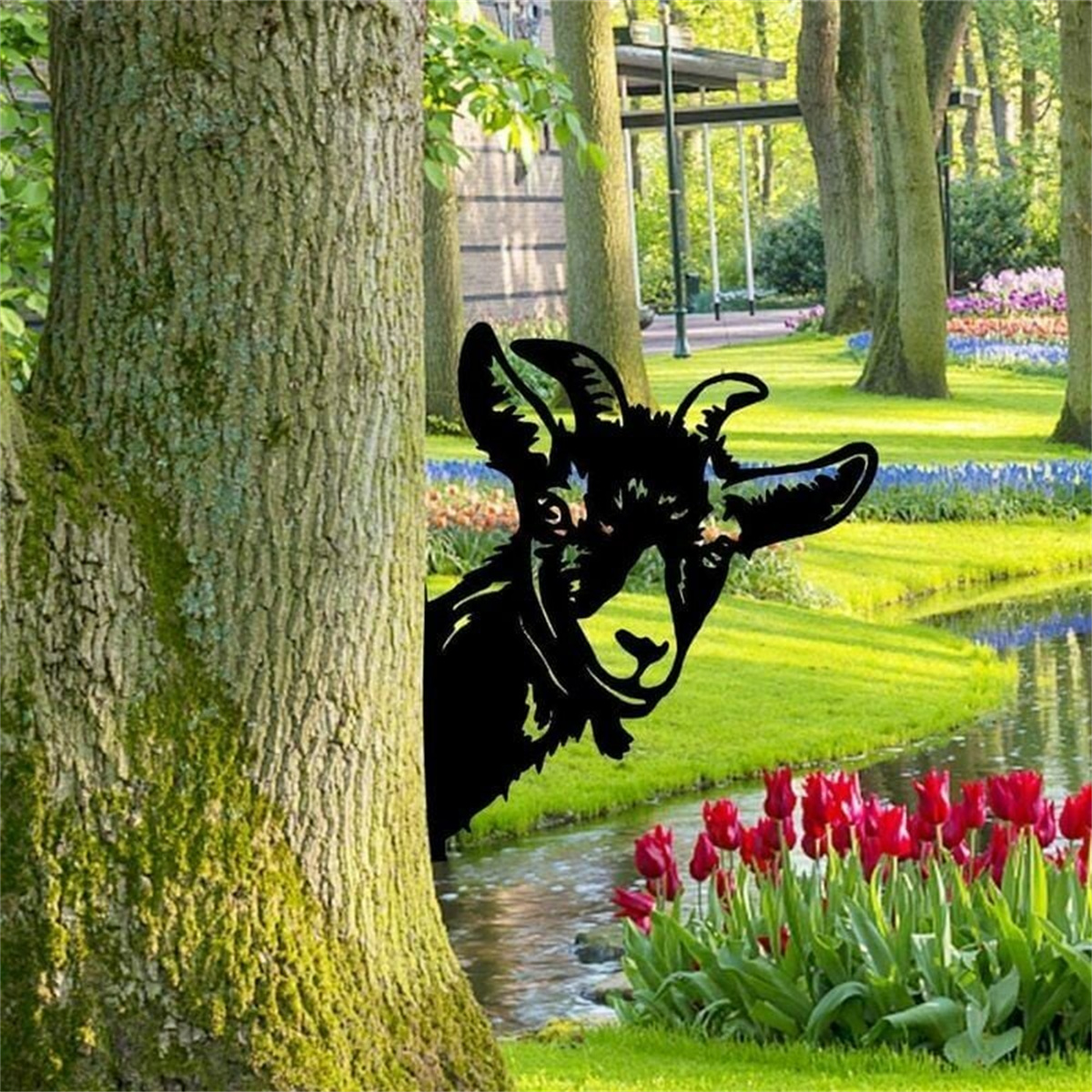 Schwarze Metallziegen-Skulptur, die hinter einem Baum hervorlugt, in der Nähe von Wasser.