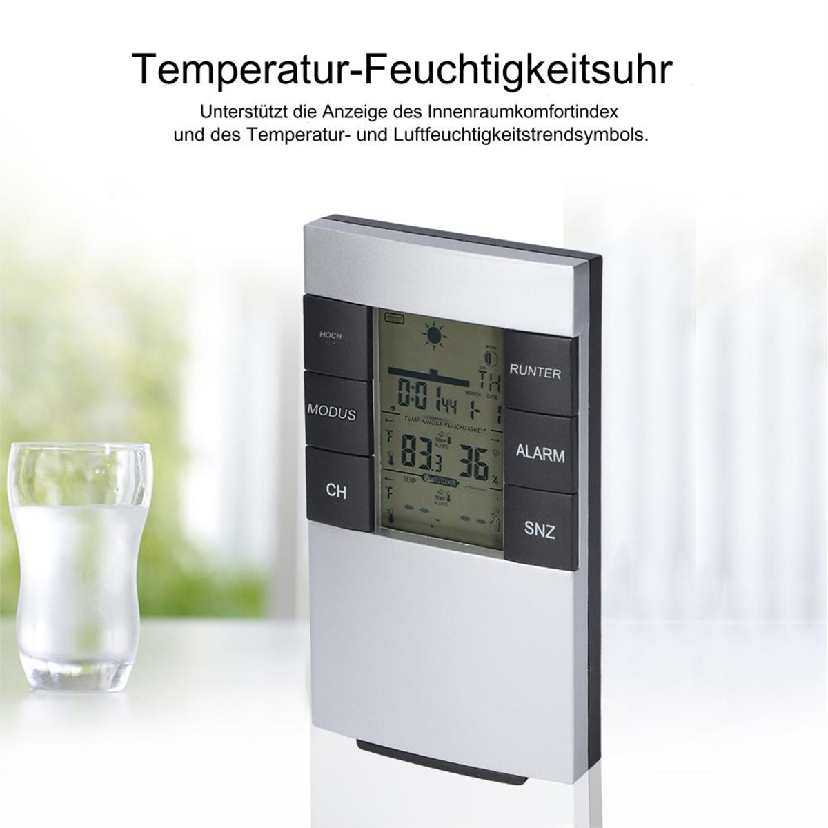 Silberne und schwarze Temperatur-Feuchtigkeits-Uhr. Sie hat ein digitales Display und mehrere Knöpfe. Links ist ein Glas Wasser.