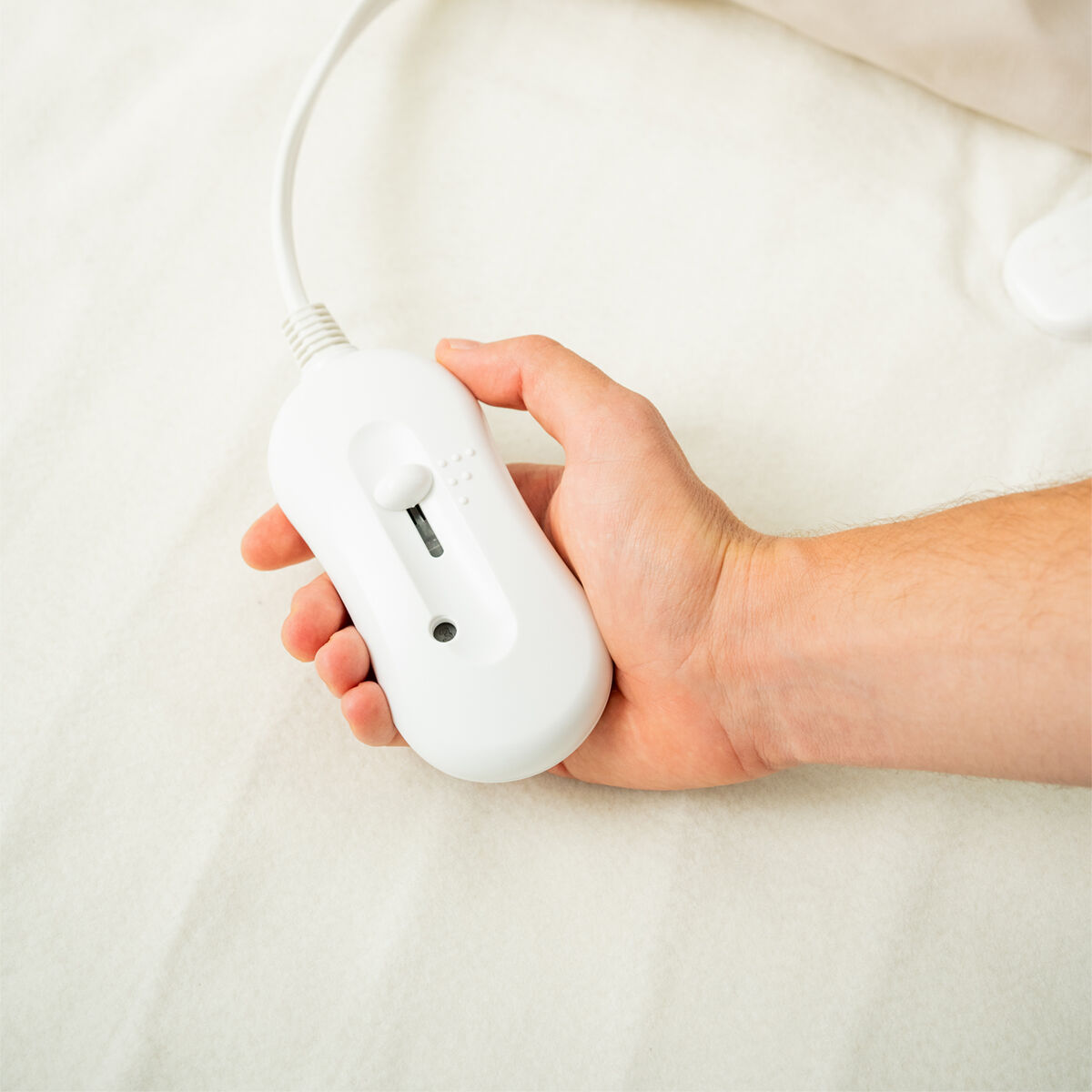 Eine Hand hält eine weiße Steuerung für eine elektrische Heizdecke. Die Decke ist beige.