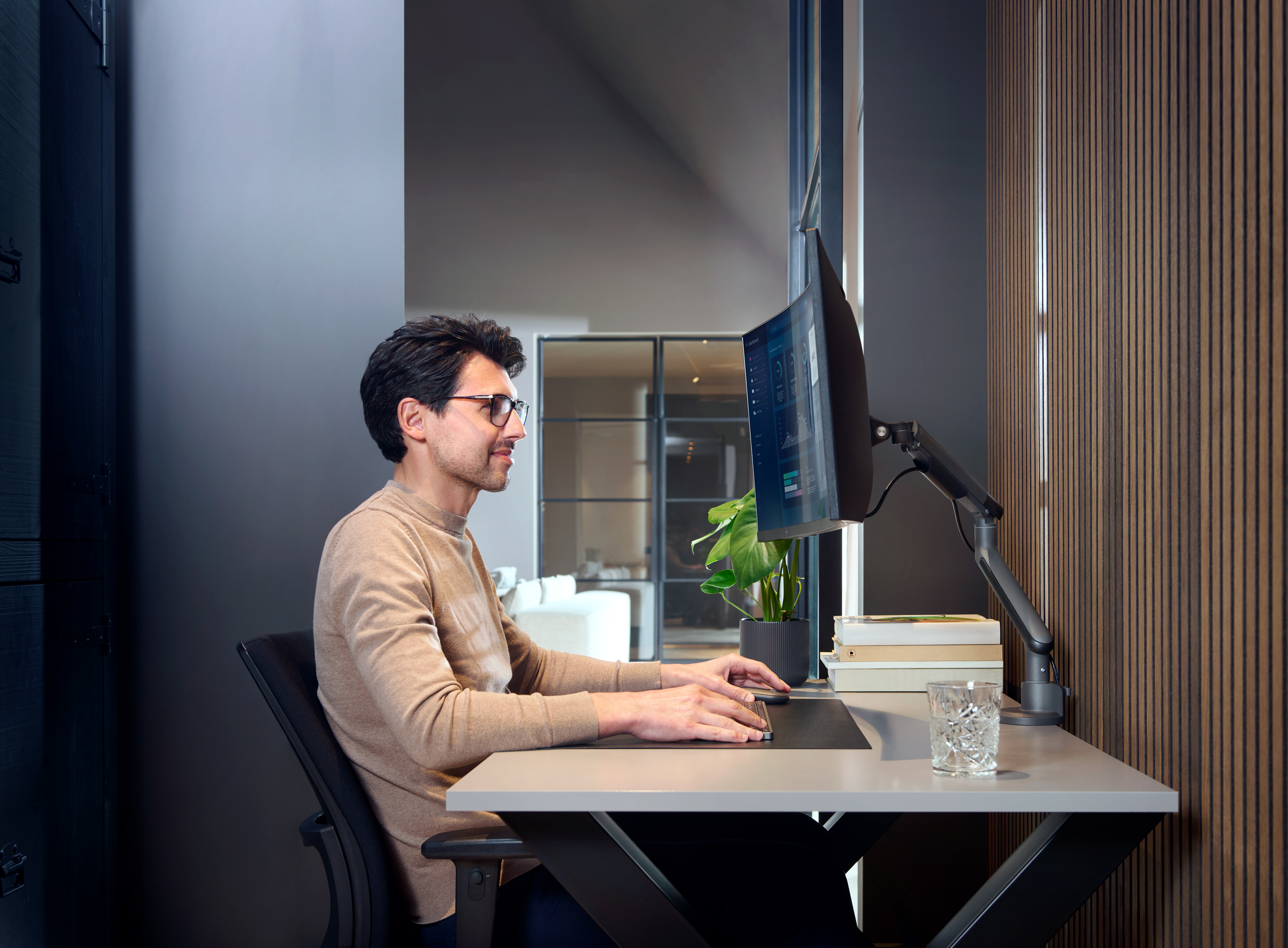 Man aan bureau met een computer met monitor. De kamer heeft een modern design.