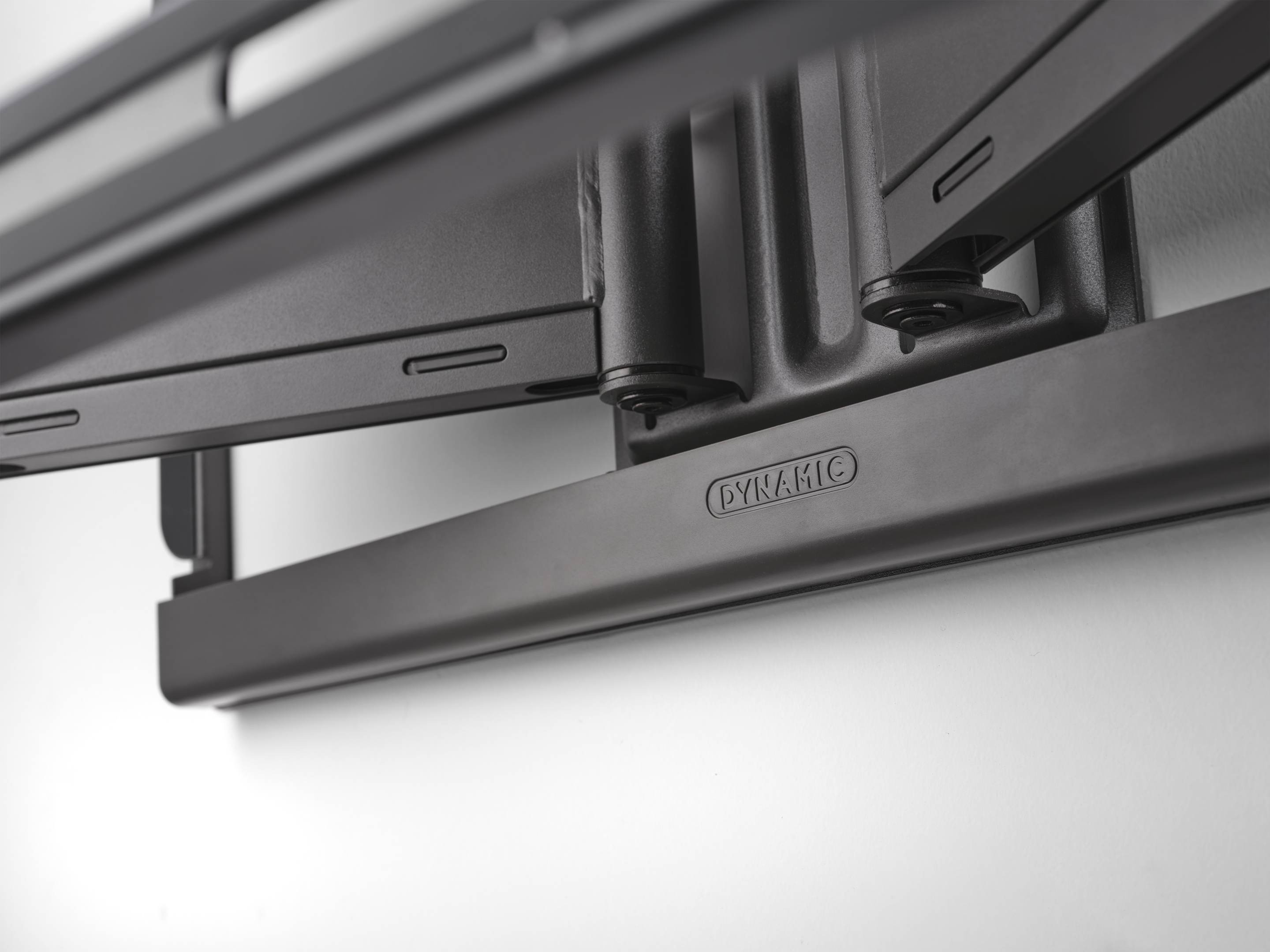 A close-up of a black, articulated TV mount on a white wall.