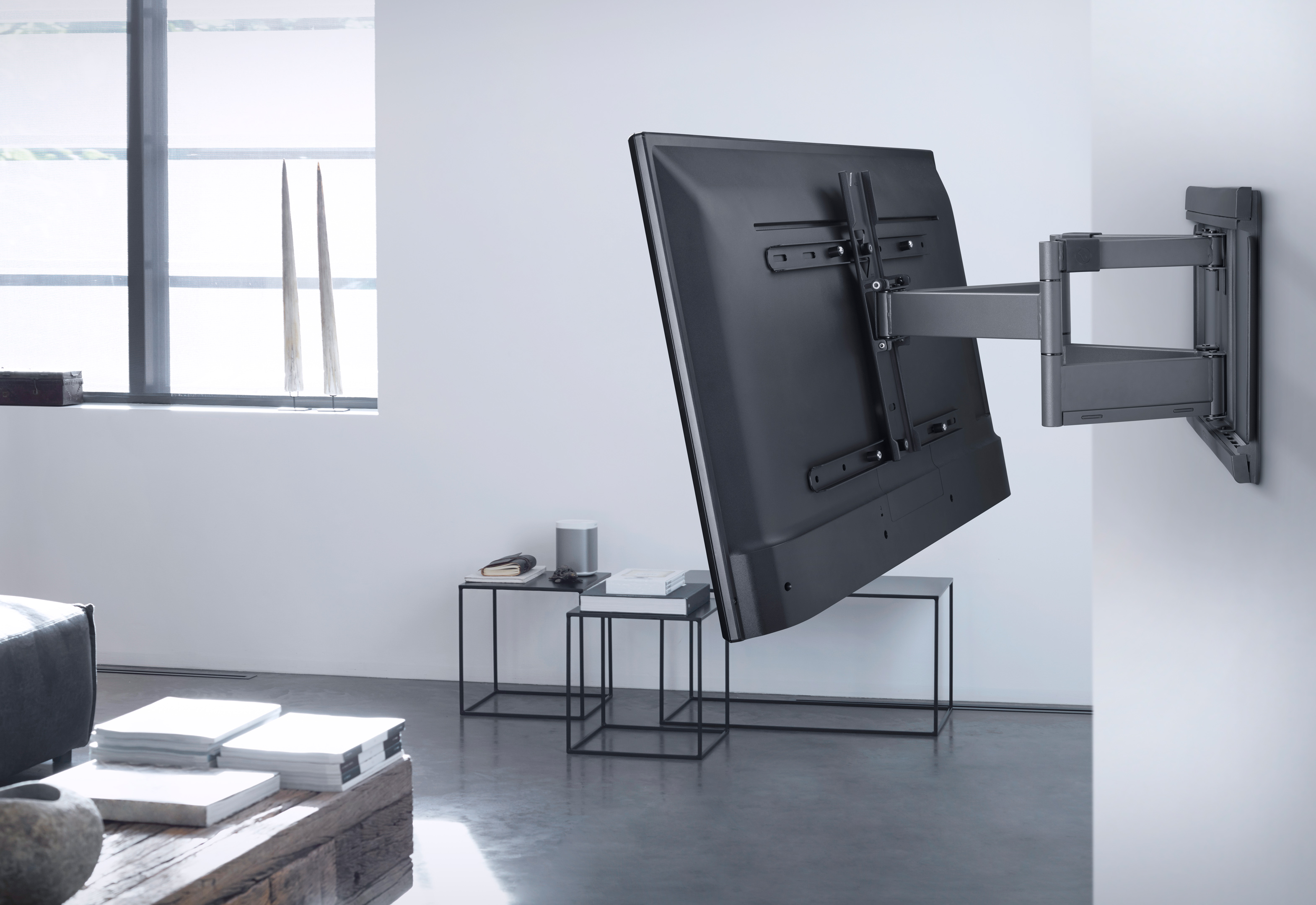 A TV mounted on a wall, swiveled to the side, with a table and decor in a living room setting.