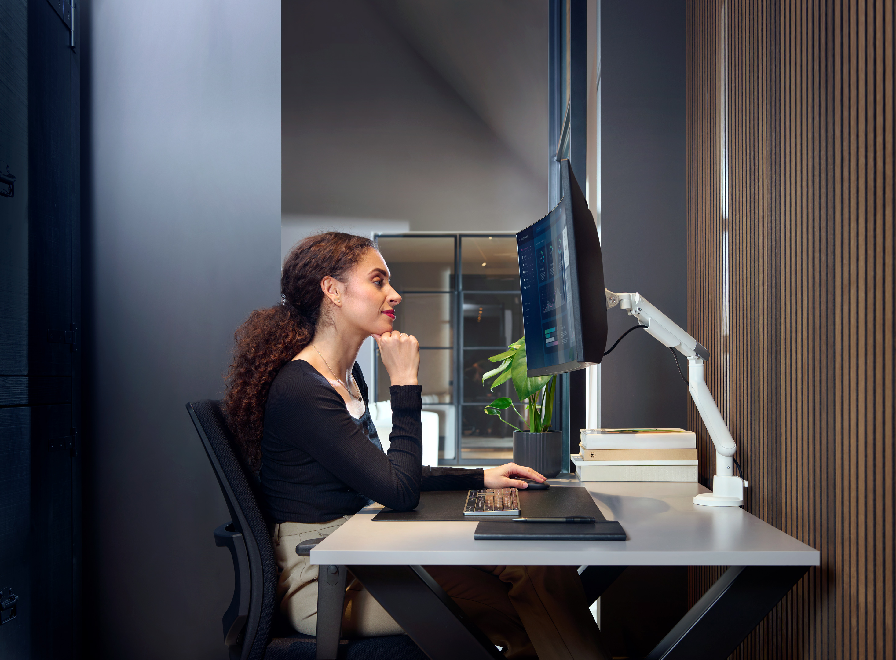 Kobieta pracująca na komputerze z ramieniem monitora. Jest w nowoczesnym biurze.
