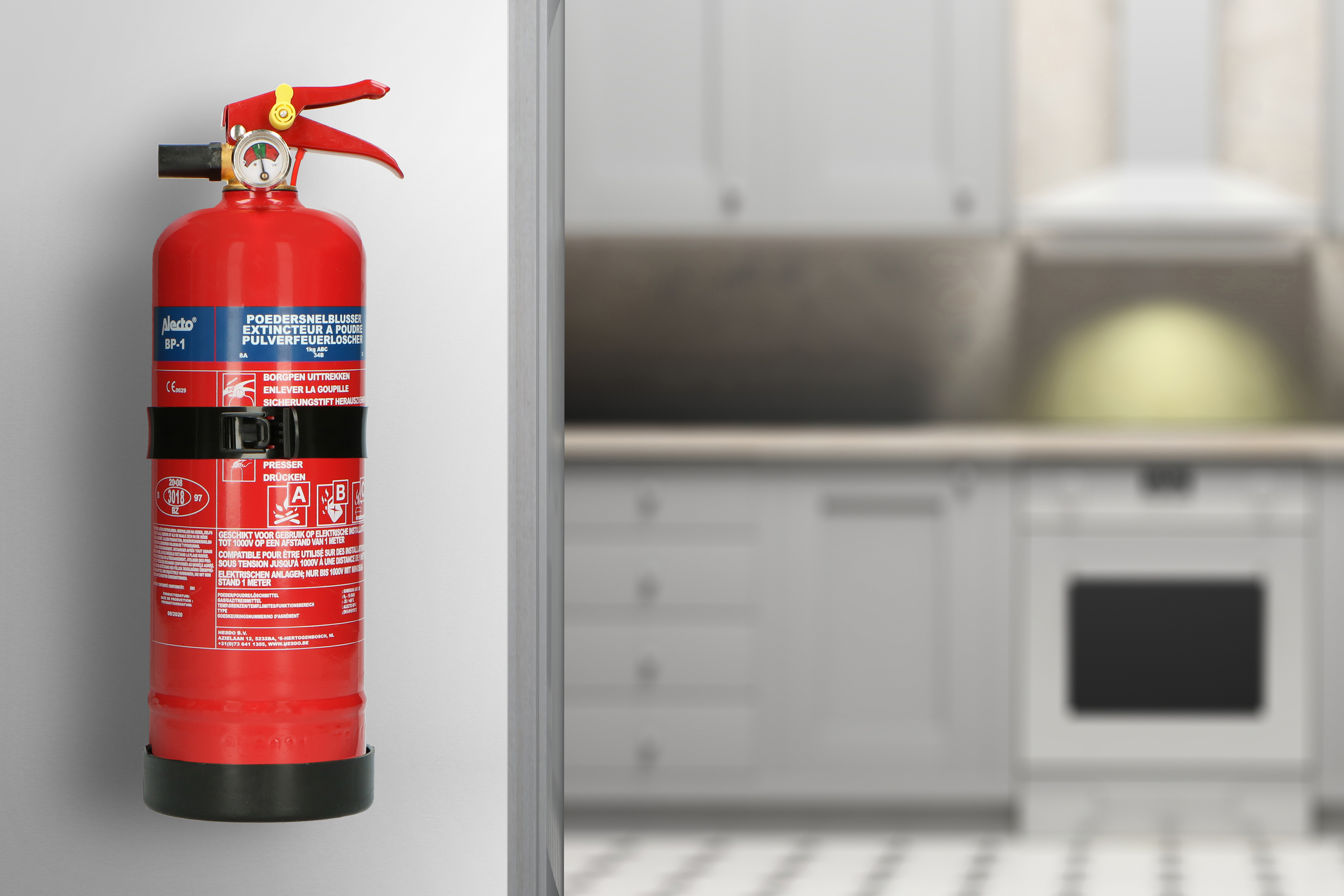 Extincteur rouge sur mur, cuisine blanche floue en arrière-plan.