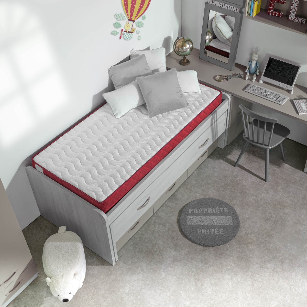 Dormitorio infantil con cama, escritorio y juguetes. Alfombra gris con escritura.