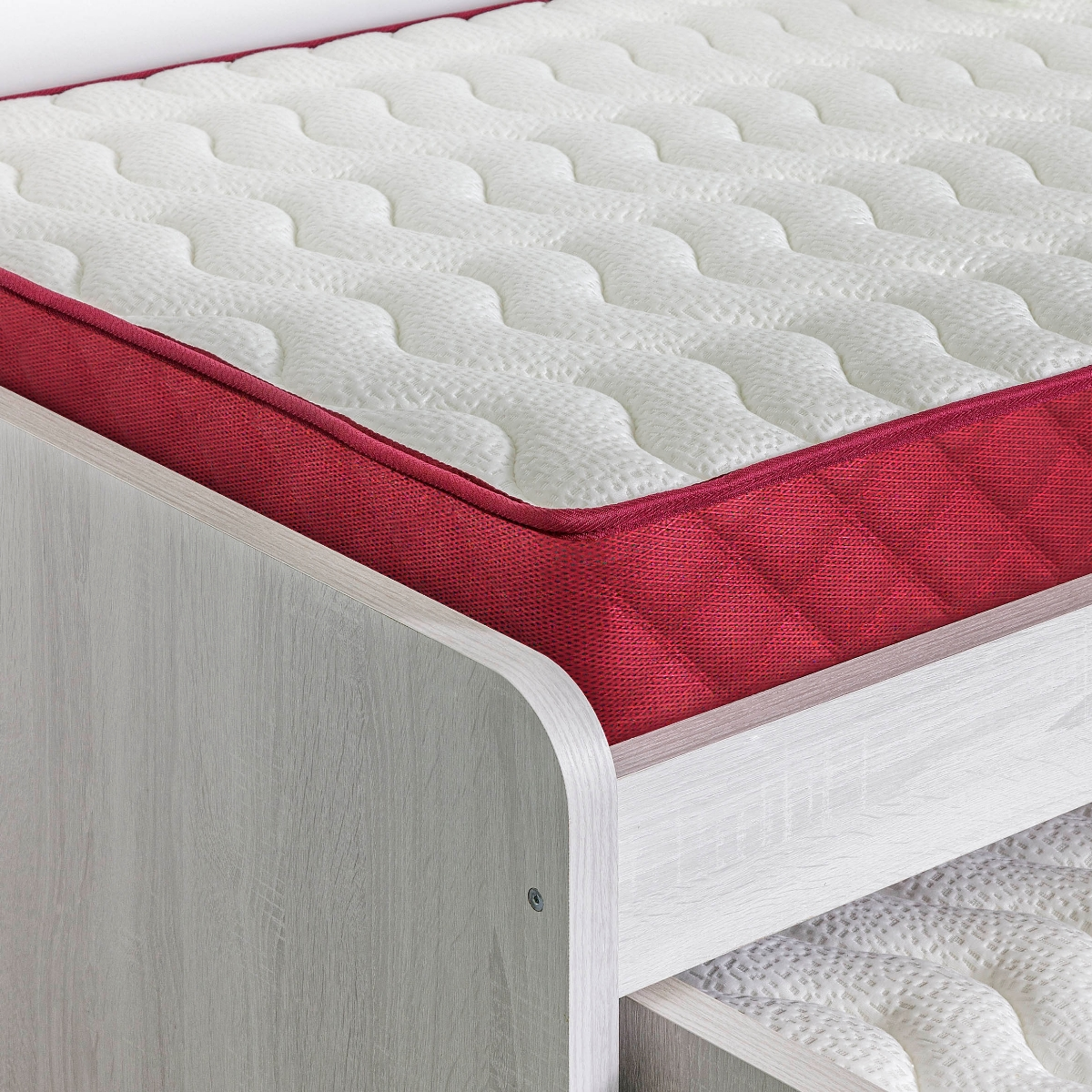 Un colchón con borde rojo y parte superior acolchada blanca. El colchón está sobre un marco de madera.