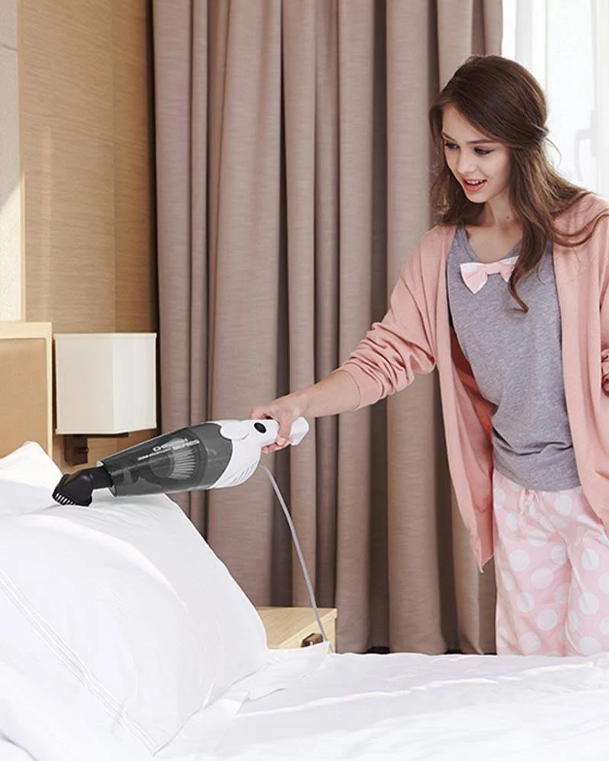 Kobieta odkurzająca łóżko urządzeniem ręcznym, w sypialni.