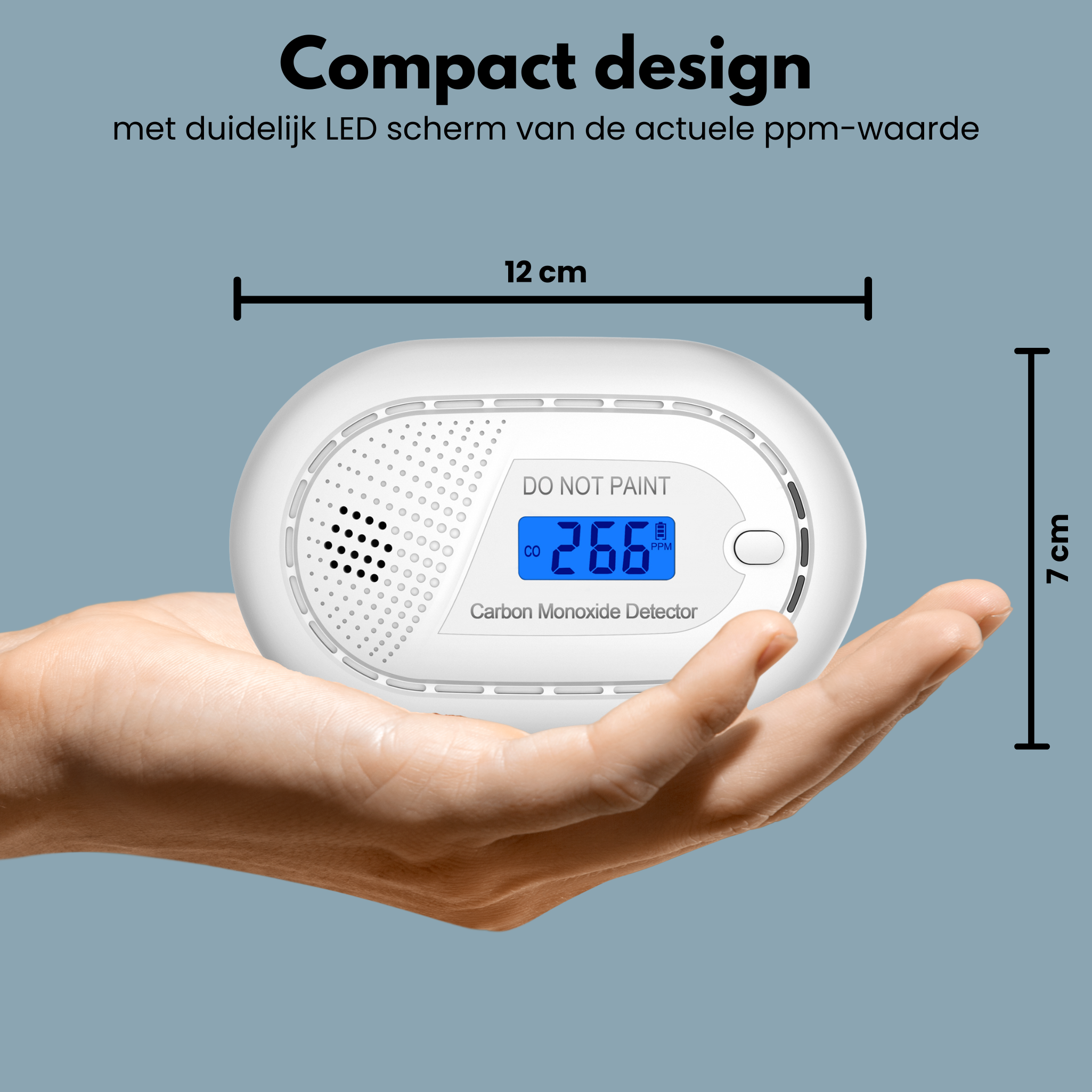 A white carbon monoxide detector held in a hand. It has a blue display. Gray background.