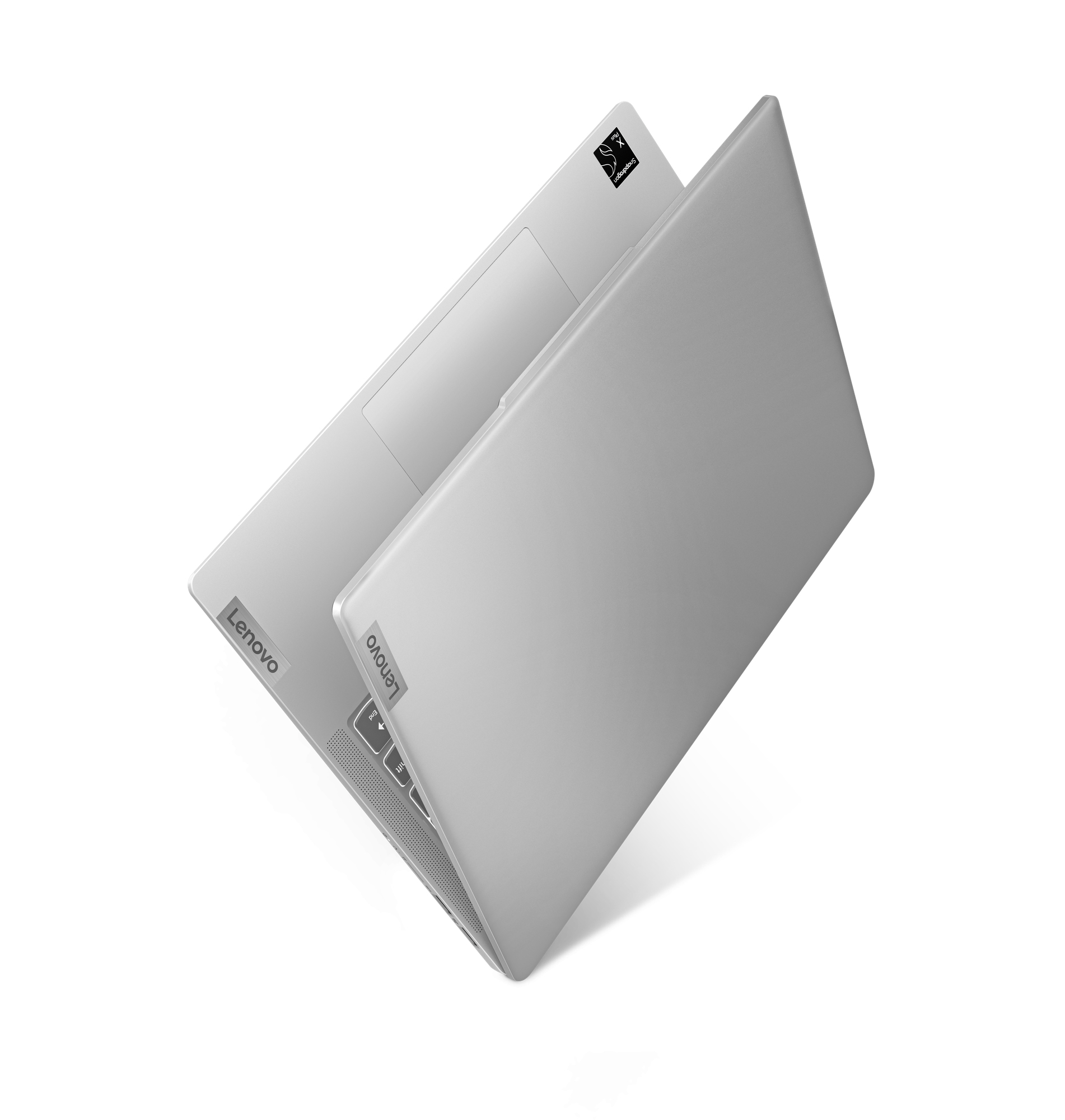 Portátil Lenovo plateado, parcialmente abierto, en una superficie blanca. Logotipo Lenovo visible.