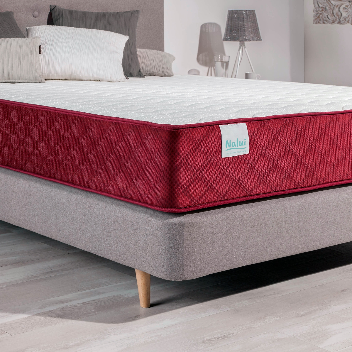 Un colchón en un marco de cama gris con borde rojo y parte superior blanca. Hay almohadas en la cama.