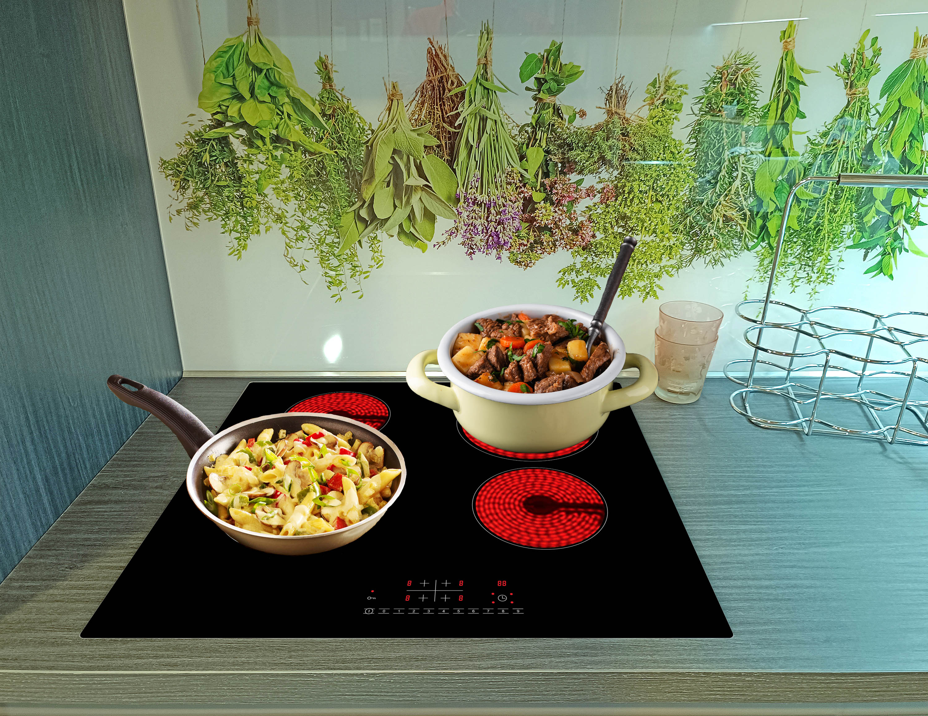 Eine Küchenszene mit einem schwarzen Kochfeld mit Essen, einem Topf mit Eintopf und hängenden Kräutern vor einer Glasrückwand.