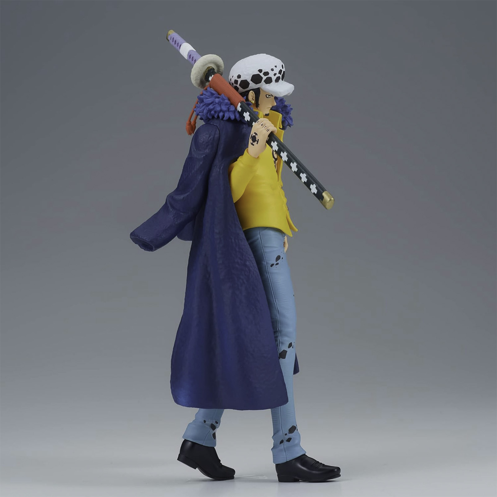 Anime-Figur eines Mannes mit Schwert, in blauem Mantel und gelbem Hemd, stehend auf einer Oberfläche.