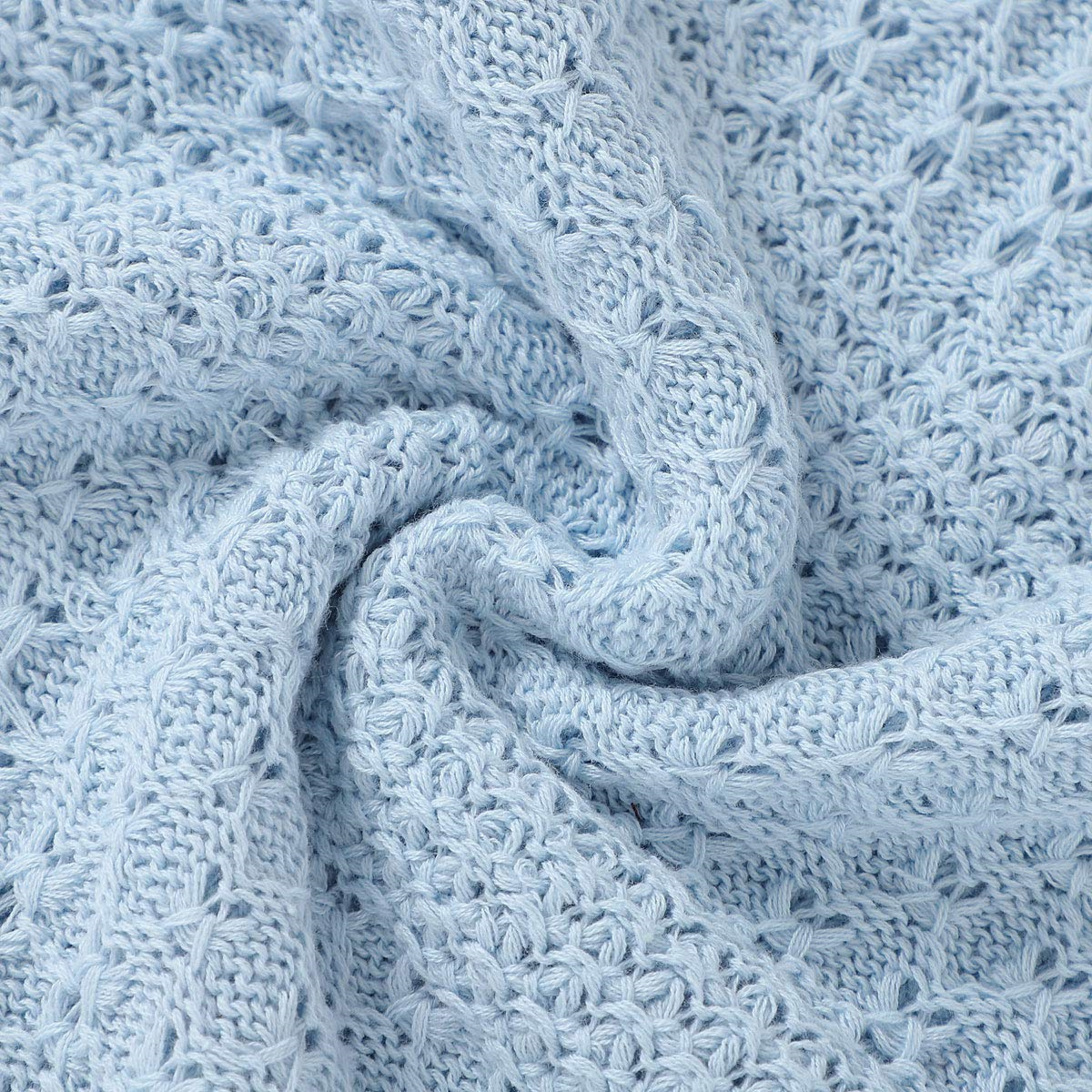 Nahaufnahme einer hellblauen Strickdecke mit strukturiertem Design, gewirbelt auf weißem Grund.
