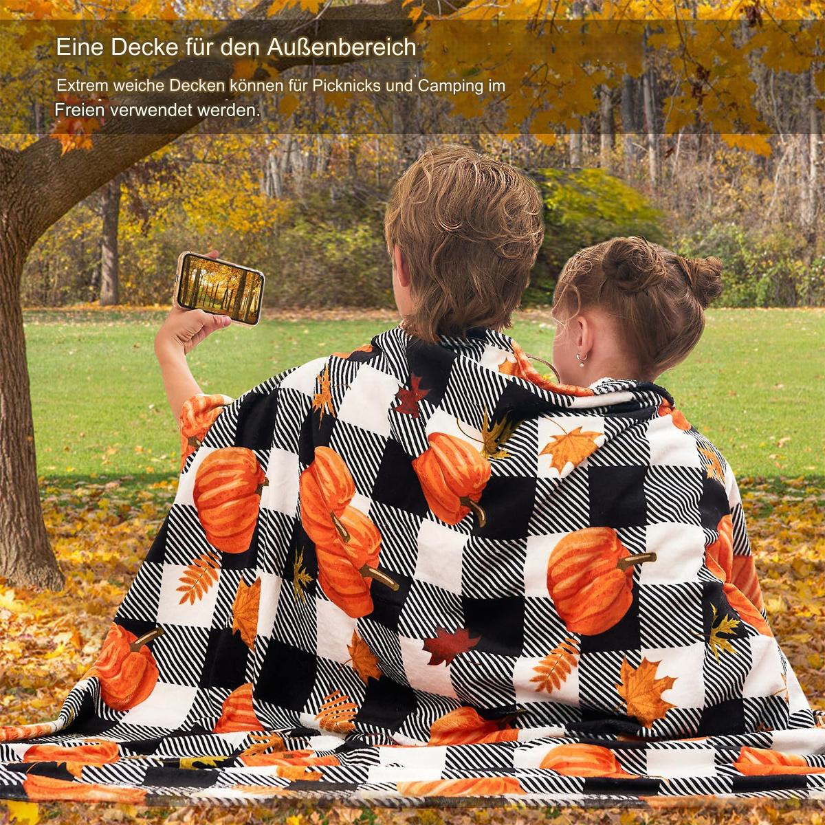 Zwei Personen in einer Kürbisdecke, eine macht ein Foto in einem Park mit Herbstlaub.