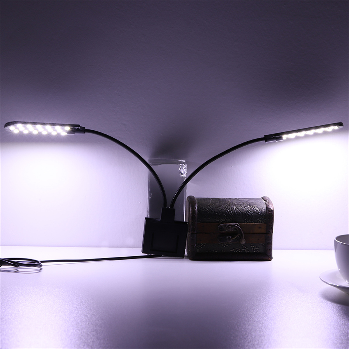 Zwei schwarze flexible Lampen mit weißen LEDs auf einem Tisch, in der Nähe einer Schatztruhe.