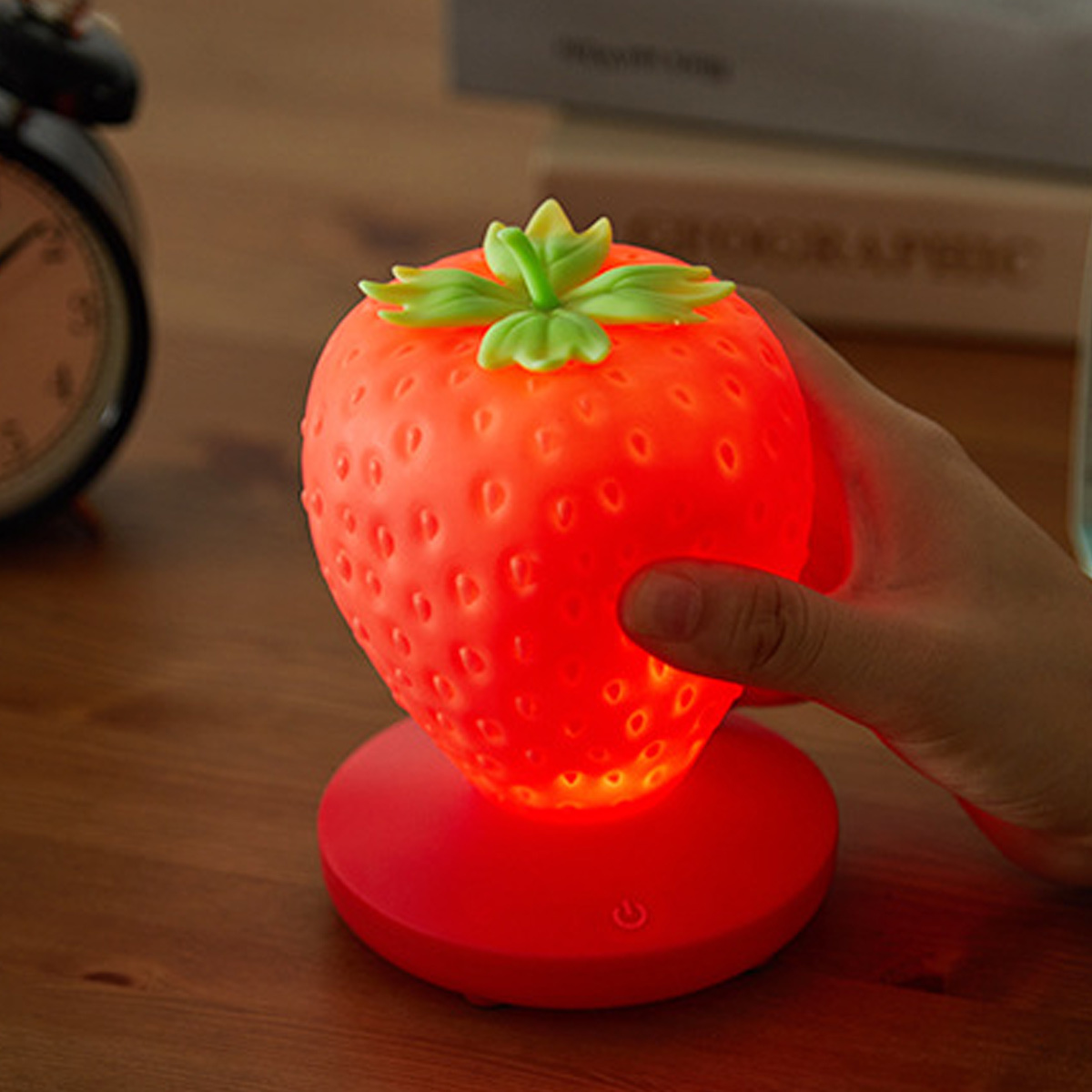 Eine erdbeerförmige Lampe, rot und grün. Hand, die die Lampe hält.