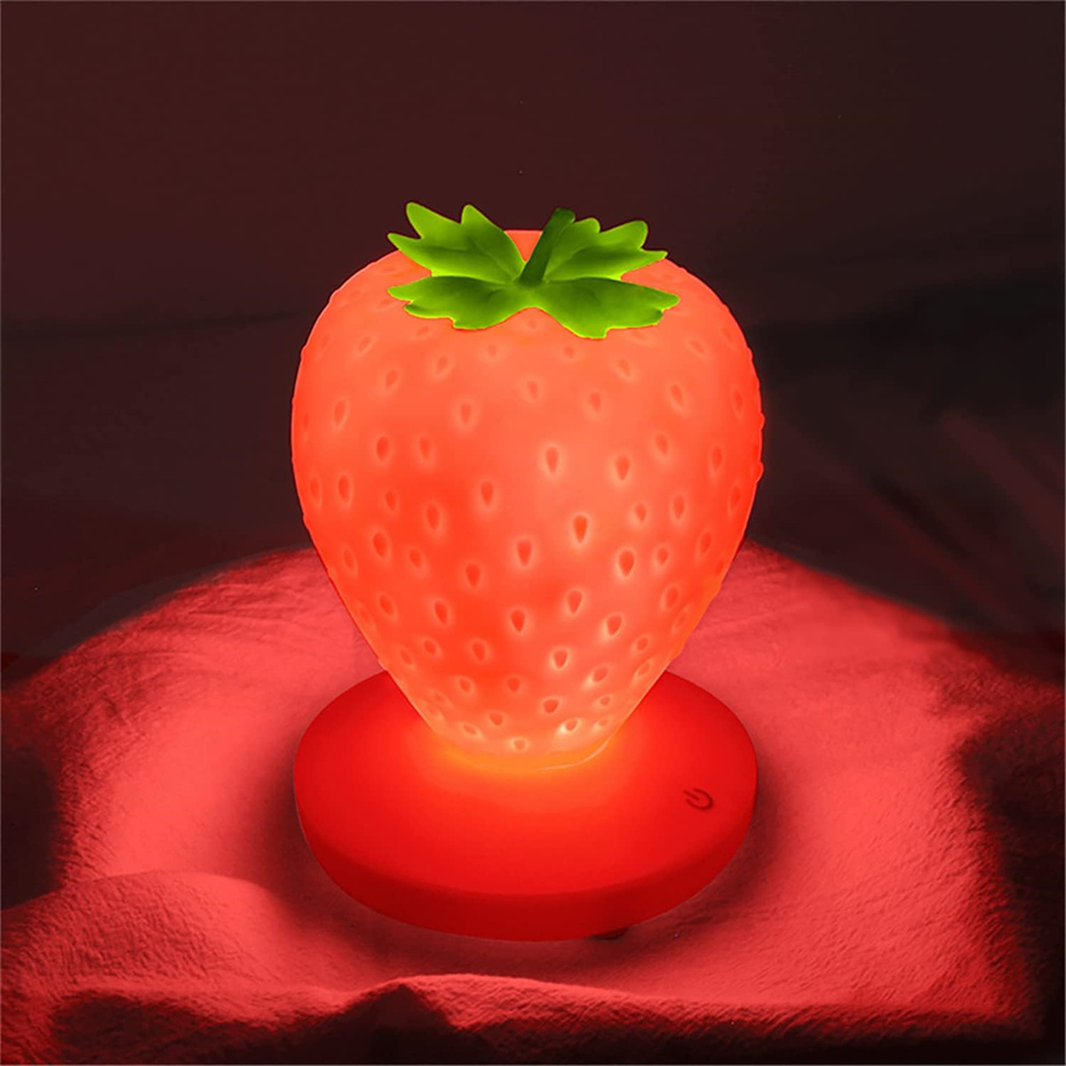 Erdbeerförmiges Nachtlicht, rot und weiß. Leuchtet mit rotem Licht auf roter Oberfläche.