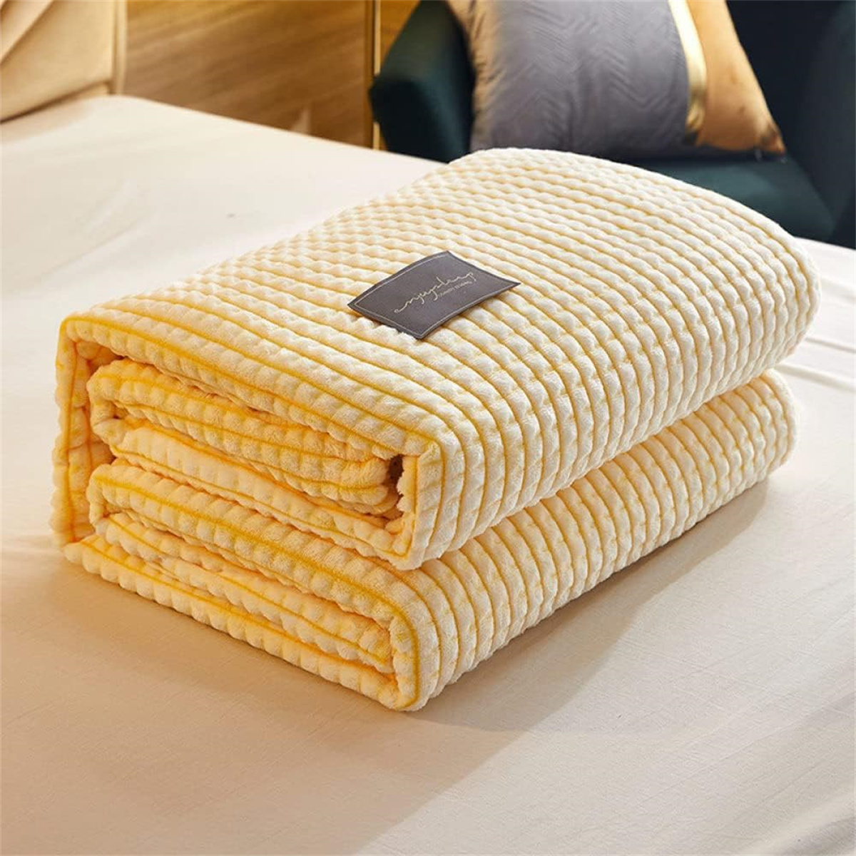 Gefaltete gelbe Decke mit einem kleinen Etikett oben. Es liegt auf einem Bett.